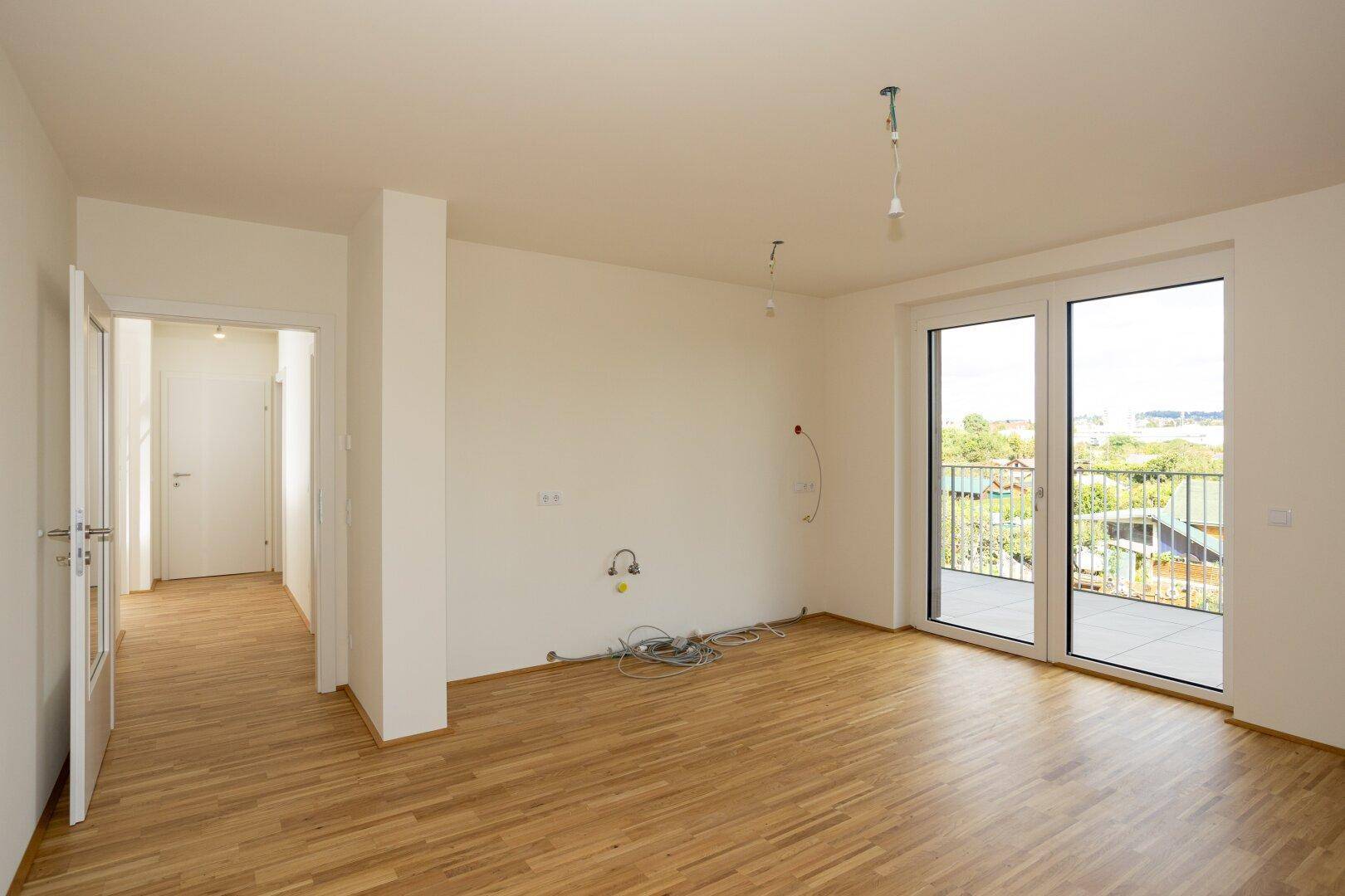 Helles Wohnzimmer mit Holzboden und Balkonzugang, bereit für die individuelle Gestaltung und Einrichtung.