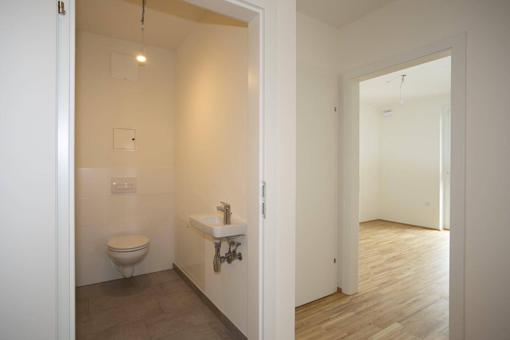 Modernes Gäste-WC mit Wand-WC und kleinem Waschbecken, in schlichtem Design gehalten.