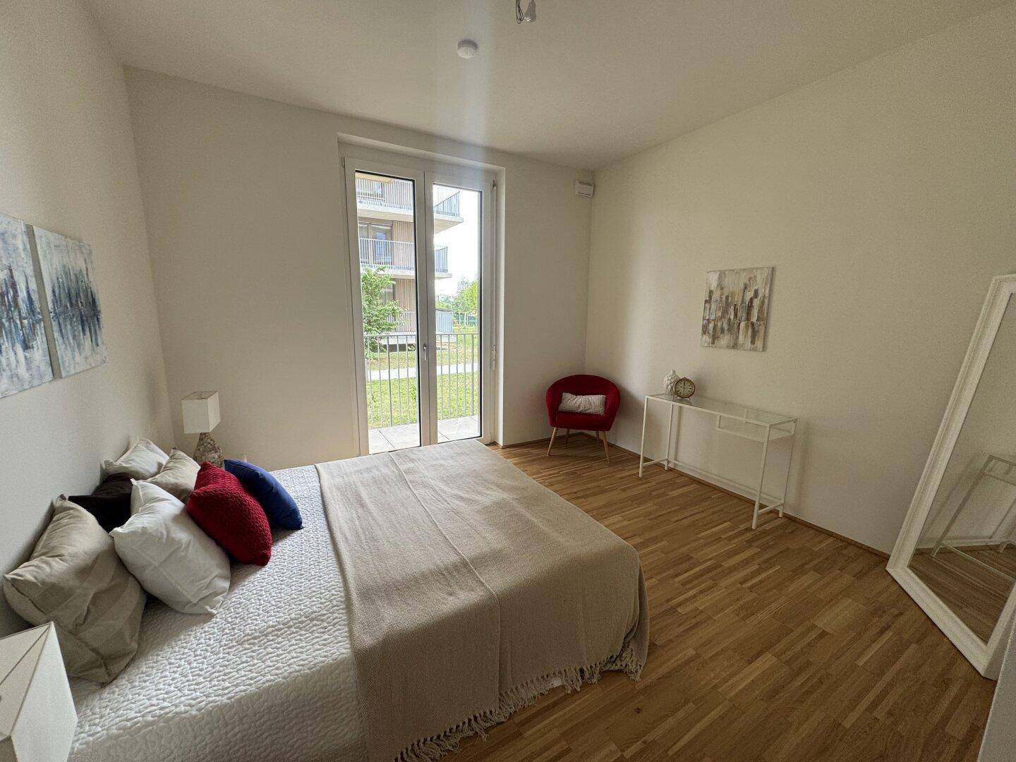 Helles Schlafzimmer mit Parkettboden und direktem Zugang zu einem Balkon oder einer Terrasse.