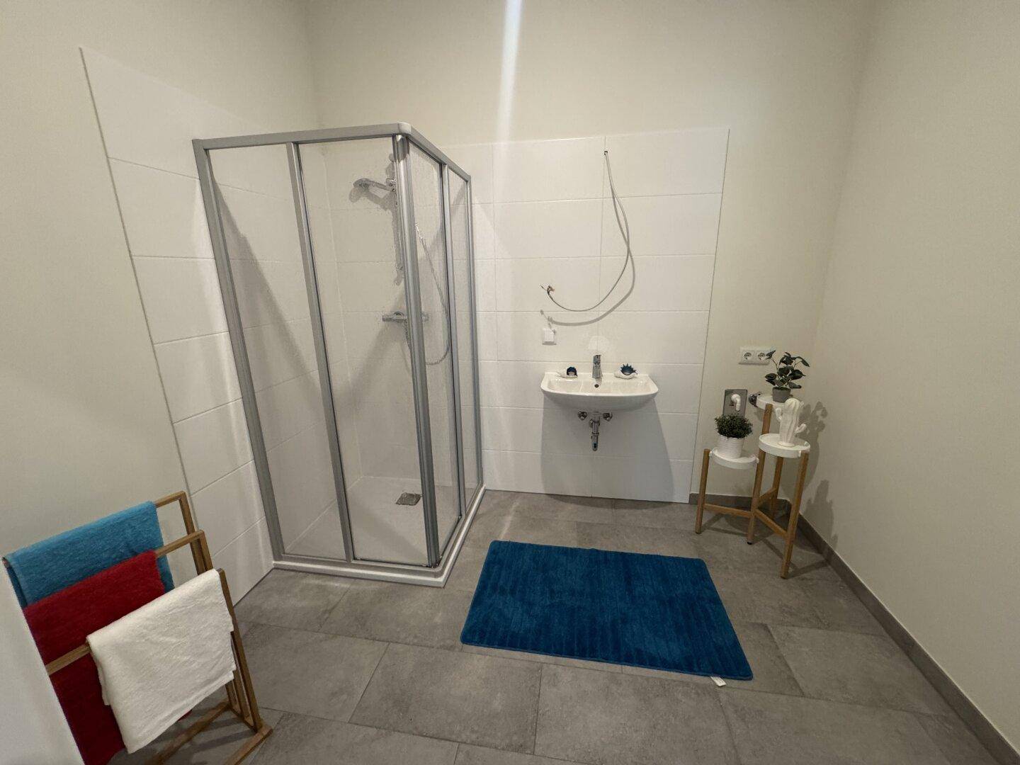 Modernes Badezimmer mit Duschkabine, Waschbecken und grauen Fliesen, funktional und hell.