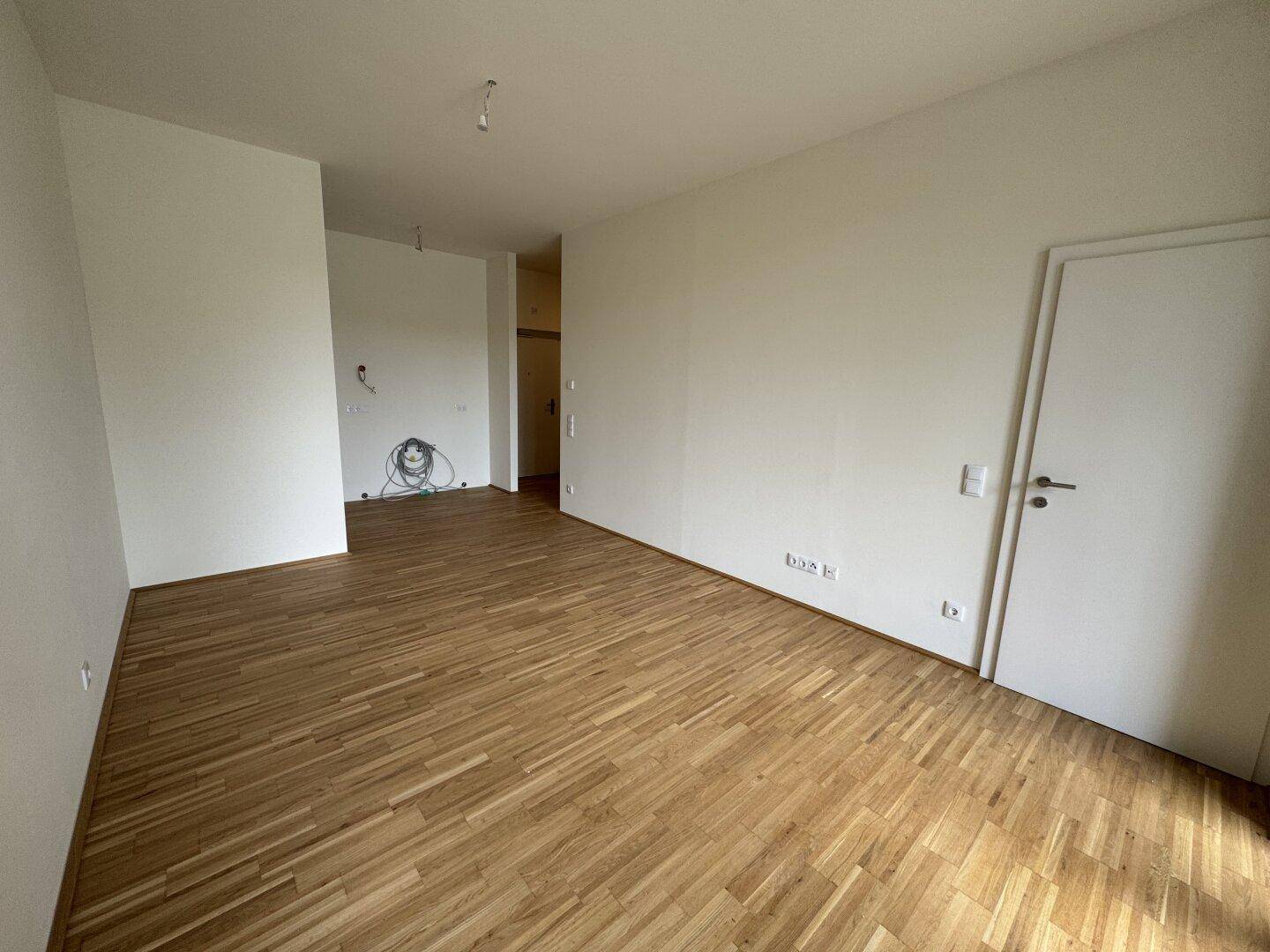 Geräumiger, unmöblierter Raum mit hellem Parkettboden und weißen Wänden, bereit zum Einzug.