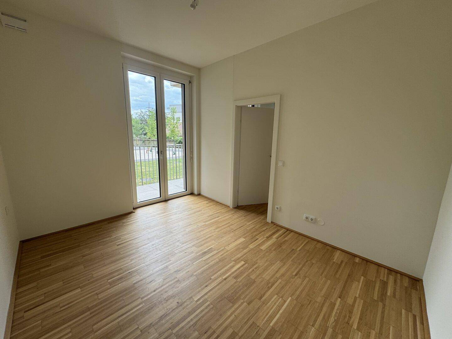 Helles Schlafzimmer mit Parkettboden und direktem Zugang zu einem Balkon.