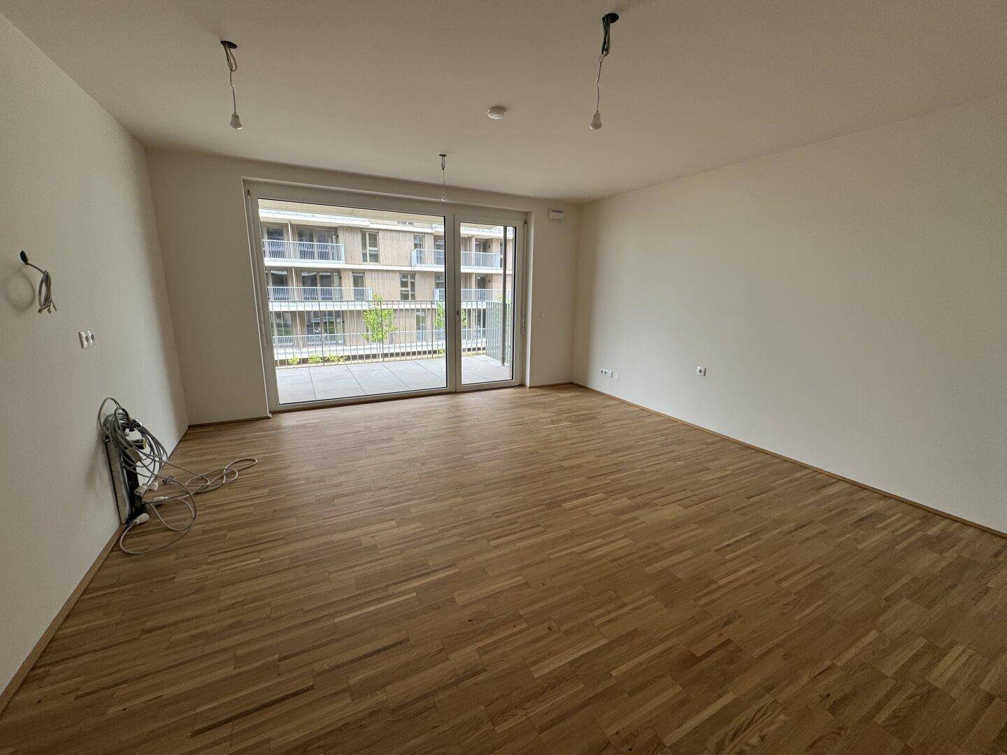 Heller, leerer Wohnraum mit Parkettboden und Zugang zu einem Balkon.