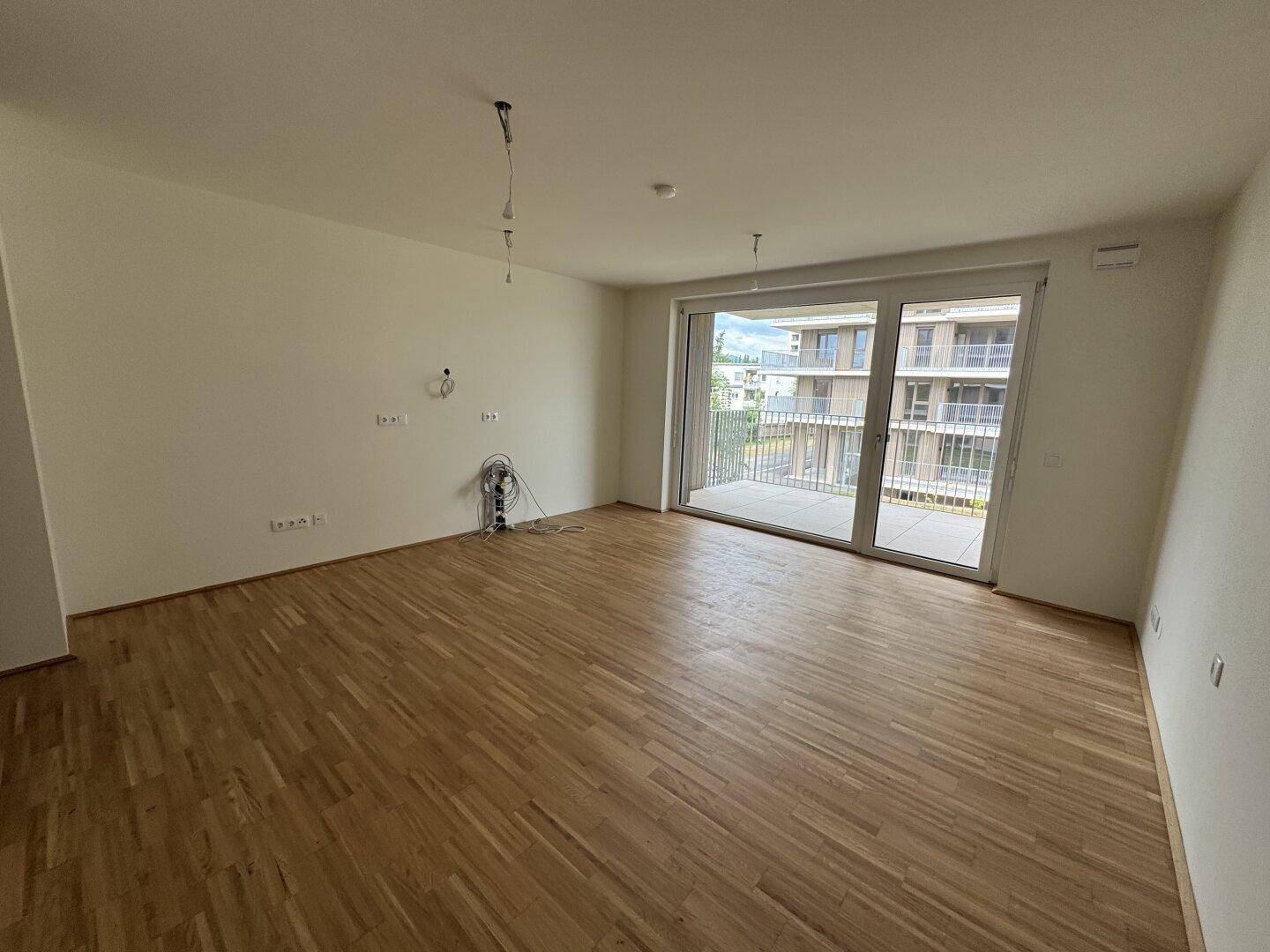 Geräumiger Wohnbereich mit hellem Parkettboden und großen Fenstern zum Balkon.