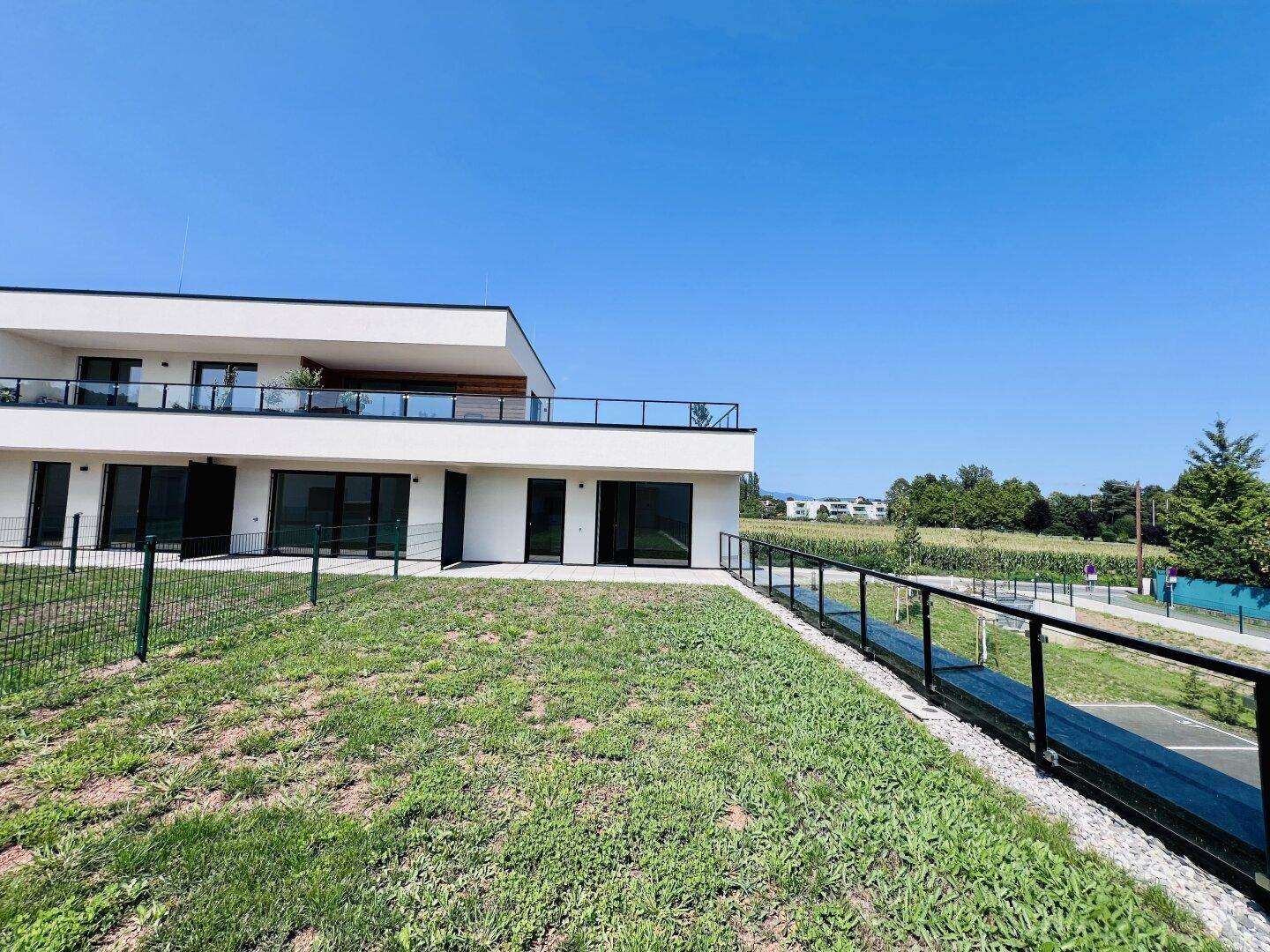 Moderne Wohnanlage mit weitläufiger Rasenfläche und Blick auf die umliegende Landschaft unter blauem Himmel.