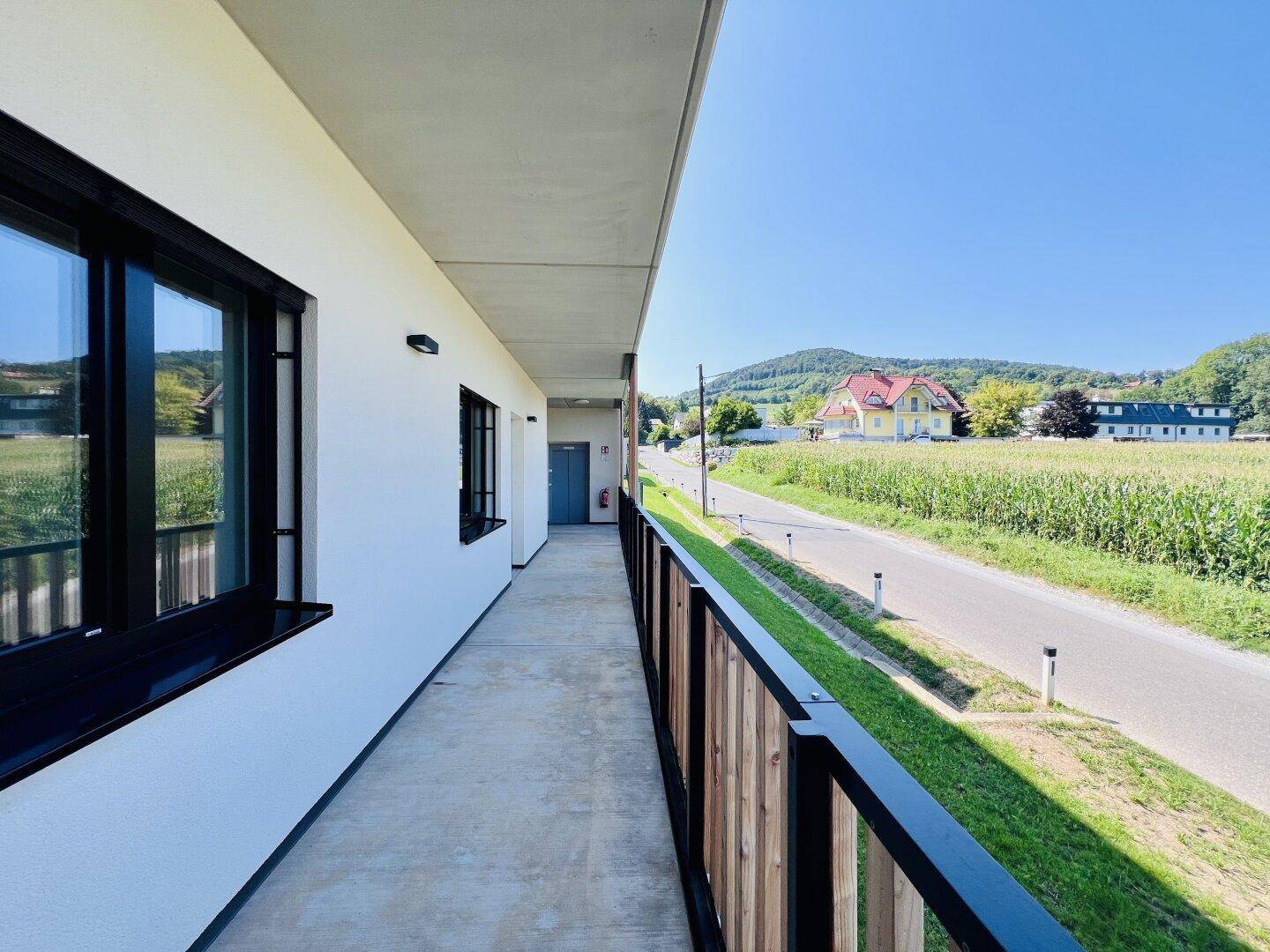 Langer Balkon mit Holzelementen und weitem Blick über Felder und die umliegende grüne Landschaft.