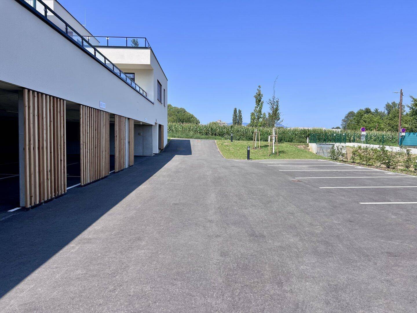 Zufahrt und Außenparkplätze vor einem modernen Gebäude mit integrierter Tiefgarage.