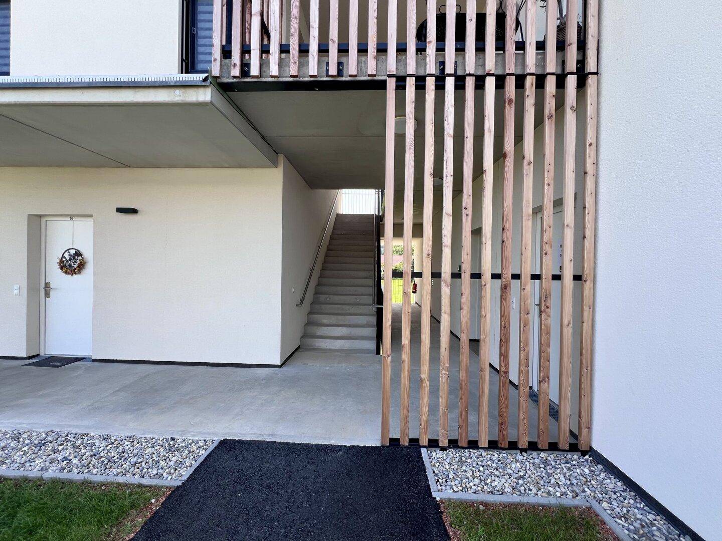 Außenbereich mit Treppenaufgang, Holzelementen und Zugang zu den Wohneinheiten der modernen Anlage.