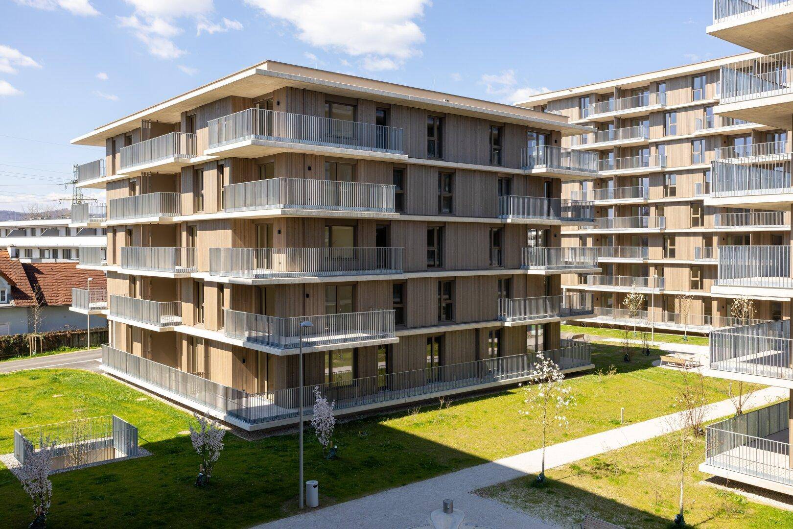 Moderne Wohnanlage mit mehreren Gebäuden, Balkonen und gepflegten Grünflächen, architektonisch ansprechend.