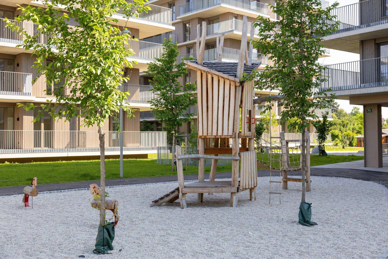 Kinderspielplatz mit Holzturm und Schaukeln in der modernen Wohnanlage, sicher und unterhaltsam.