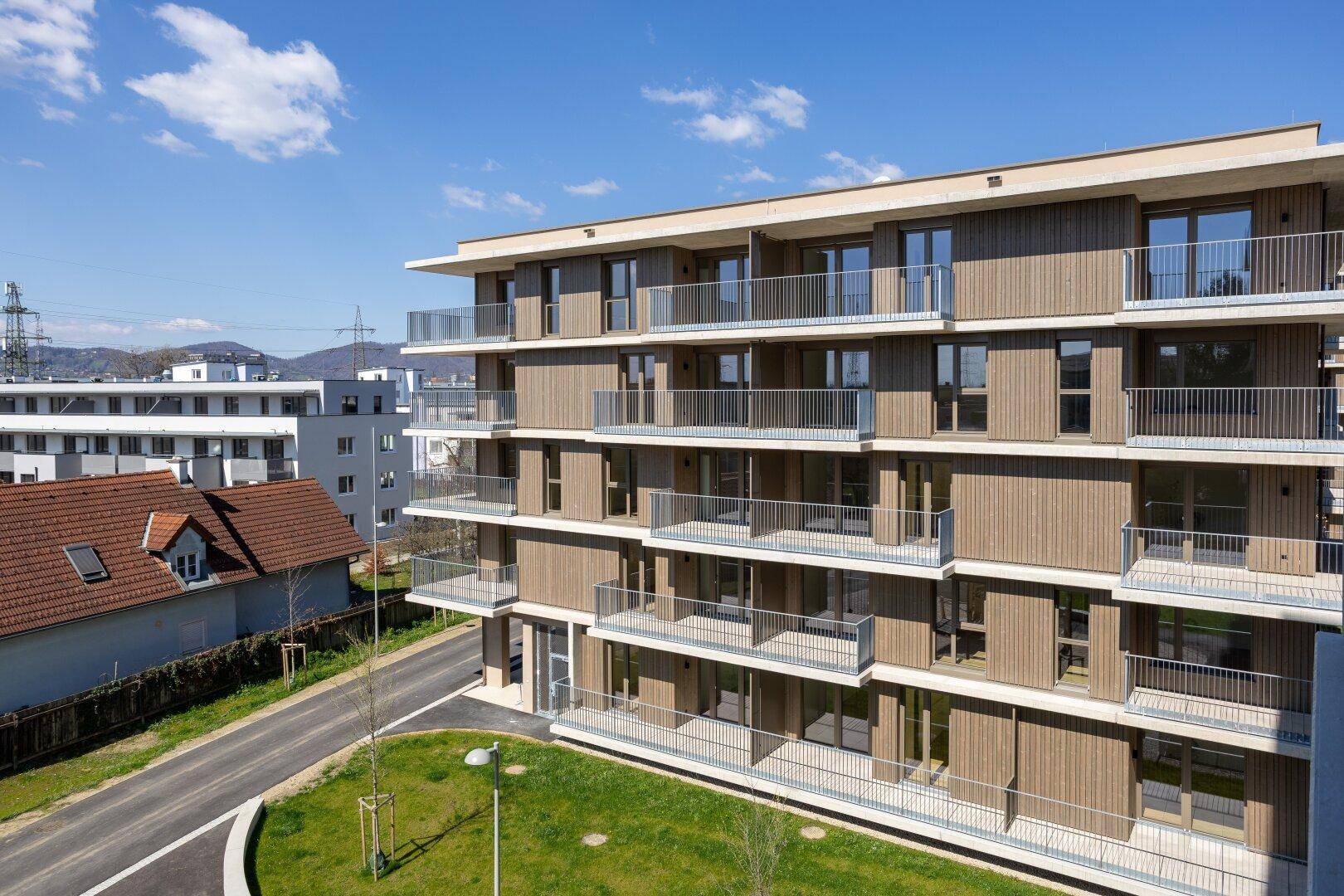 Moderne Wohngebäude mit Holzfassade und Balkonen unter blauem Himmel, harmonisch in die Umgebung integriert.