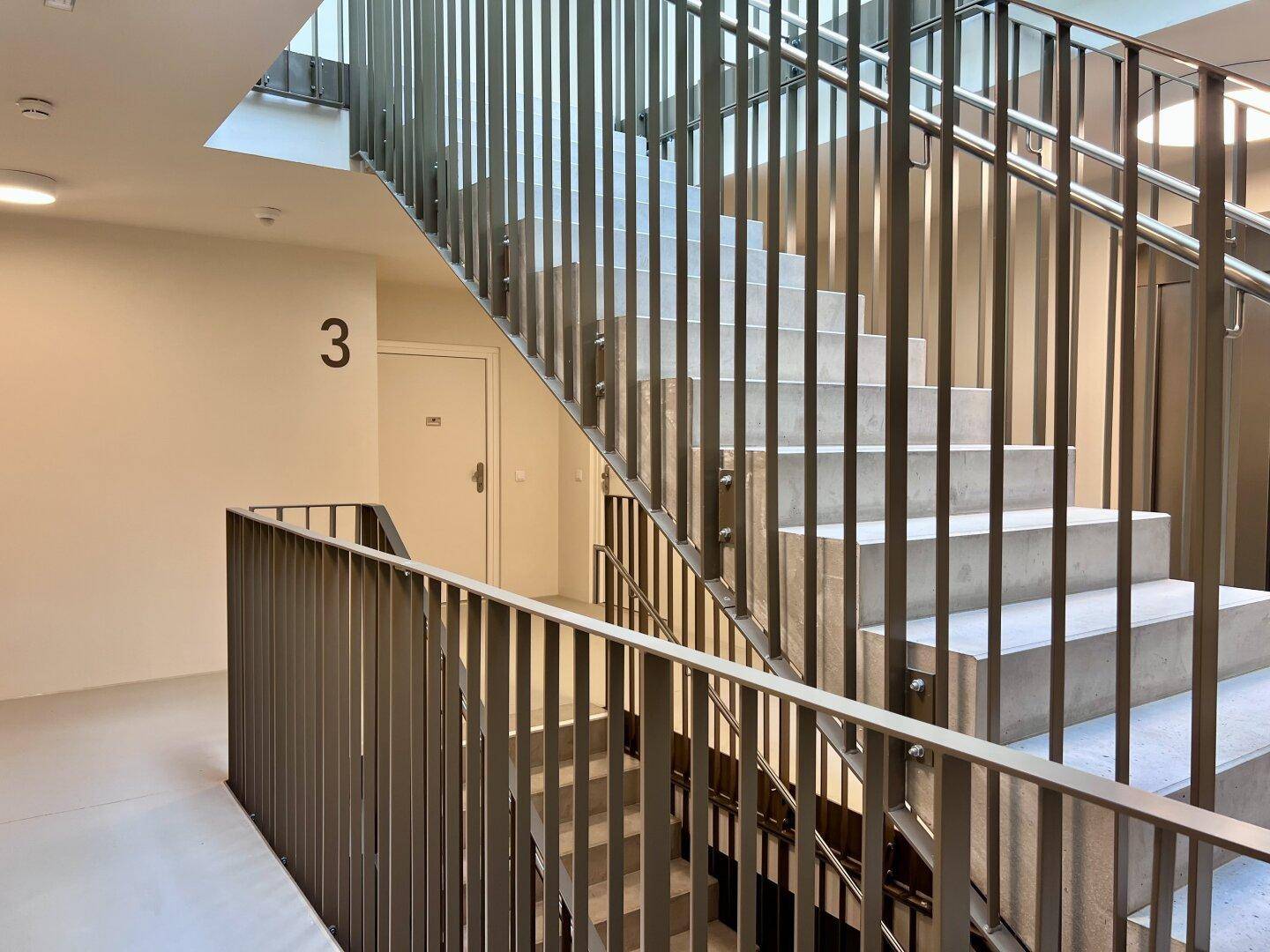 Modernes Treppenhaus mit Metallgeländer und hellen Stufen, gut beleuchtet und zugänglich.