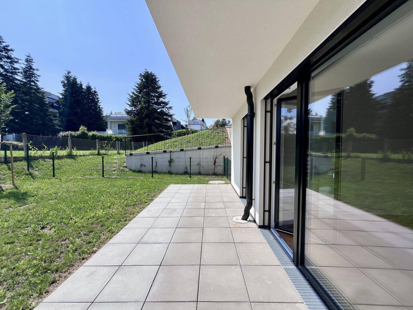 Geräumige, gepflasterte Terrasse mit großen Glasschiebetüren und Zugang zu einer Rasenfläche.
