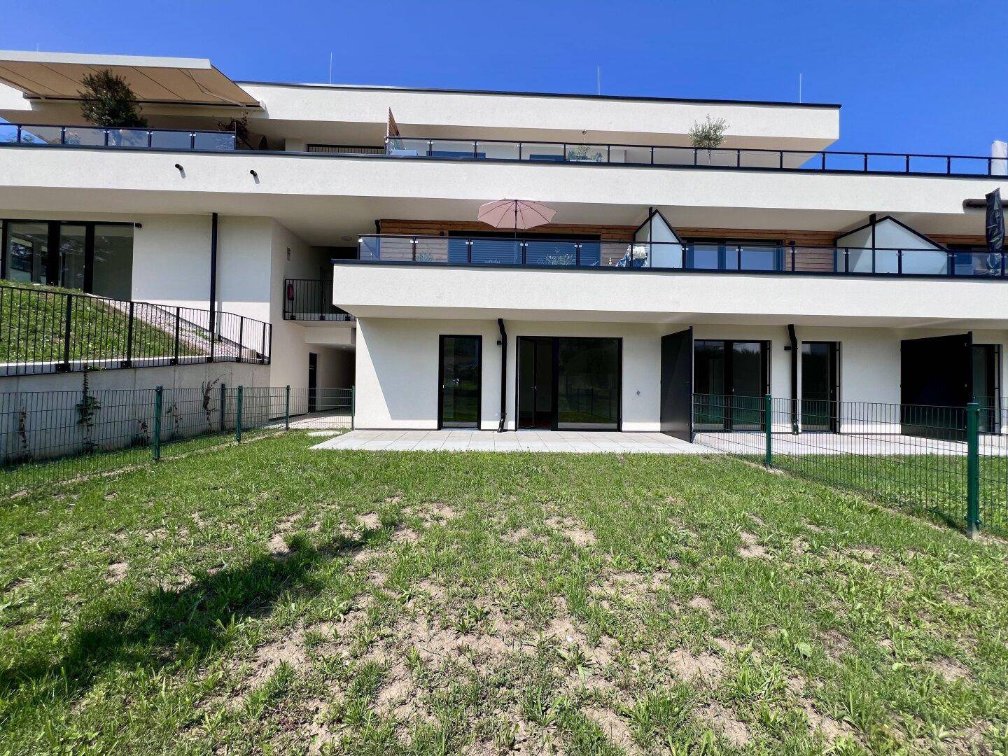 Moderne Wohnanlage mit Terrassen und Gartenflächen im Erdgeschoss sowie Balkonen in den oberen Etagen.