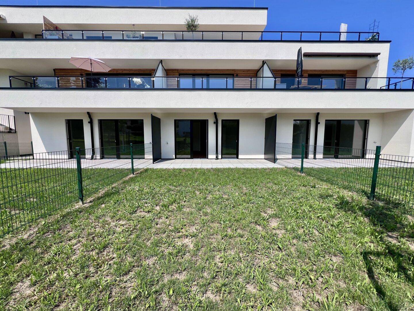Moderne Wohnanlage mit mehreren Terrassen und einem weitläufigen Gartenbereich im Vordergrund.