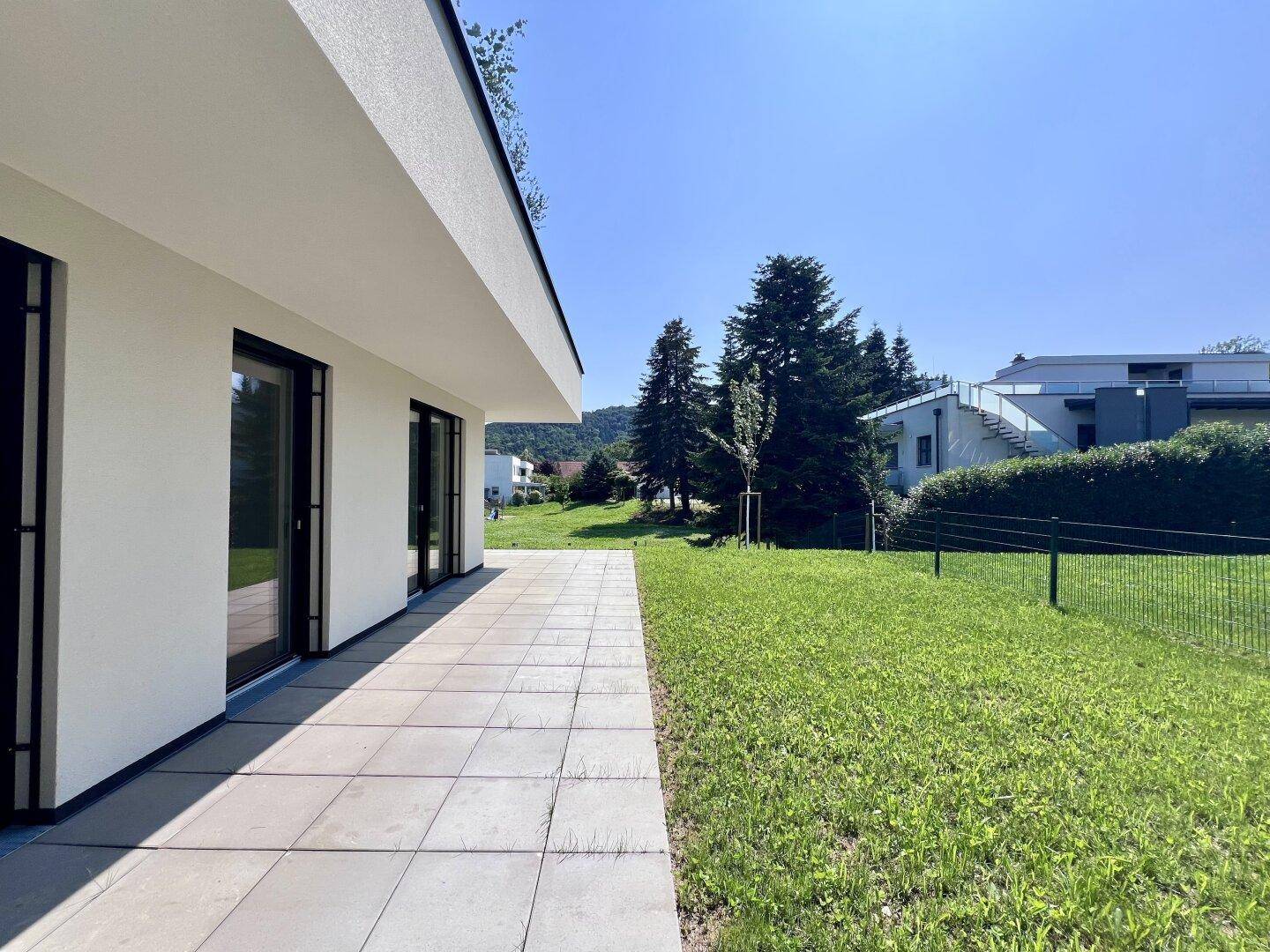 Großzügige Rasenfläche neben einer modernen Terrasse mit Blick ins Grüne.