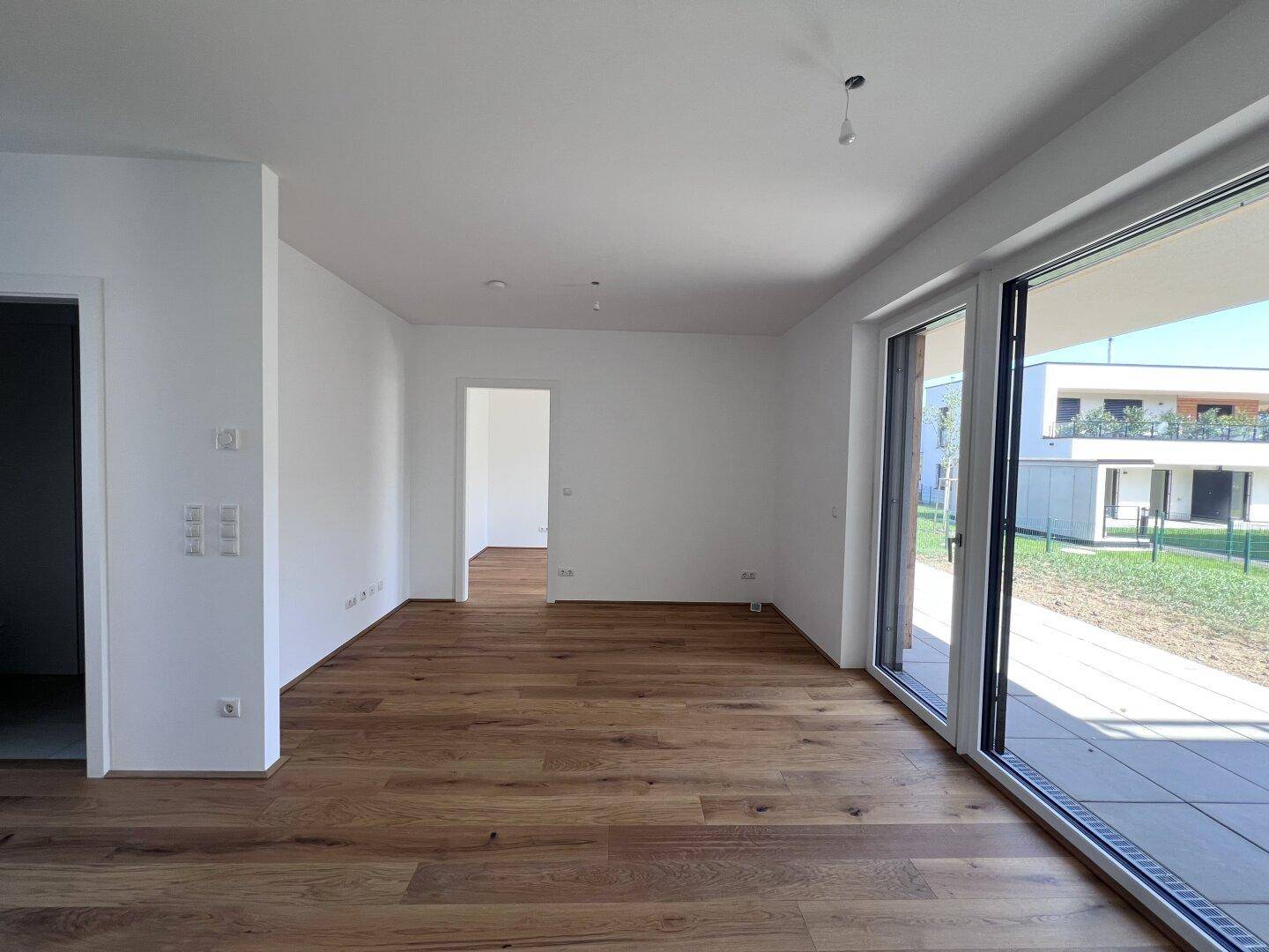 Heller, leerer Wohnraum mit Eichenparkettboden und großen Schiebetüren zur Terrasse.