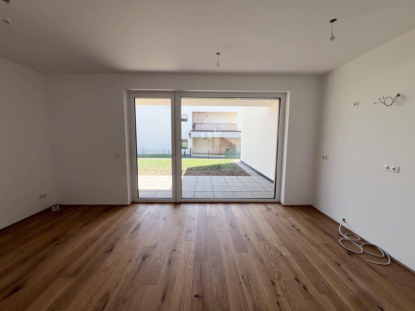 Geräumiger, unmöblierter Wohnbereich mit Holzboden und Blick auf den Innenhof.