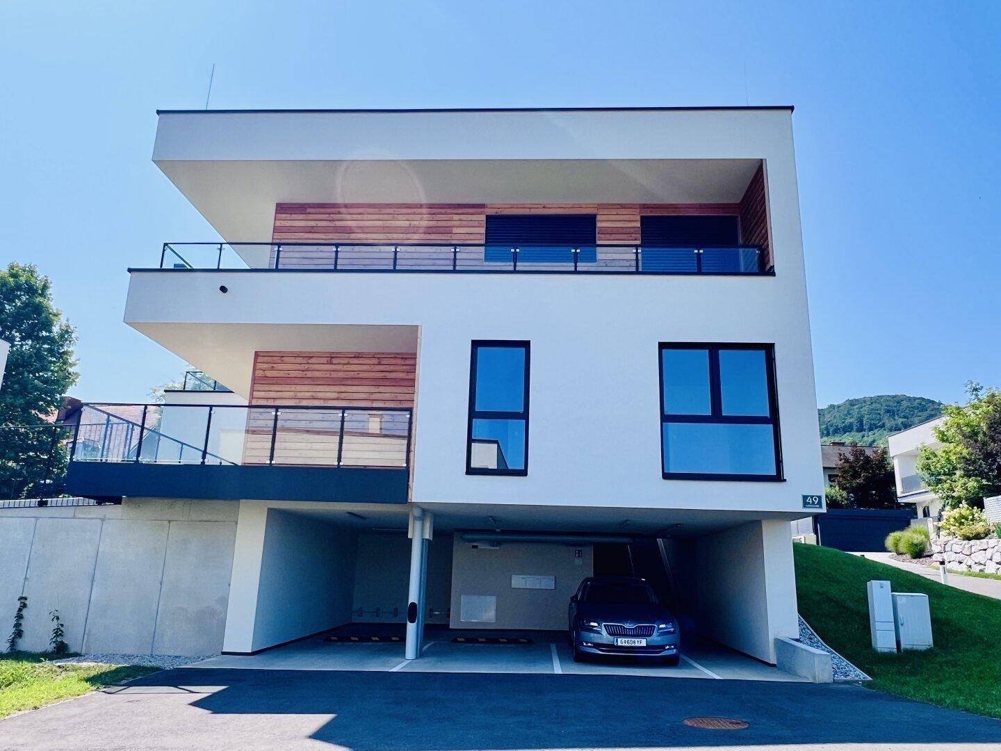 Moderne Wohnanlage mit weißer Fassade, großen Fenstern und integrierten Parkplätzen im Erdgeschoss.