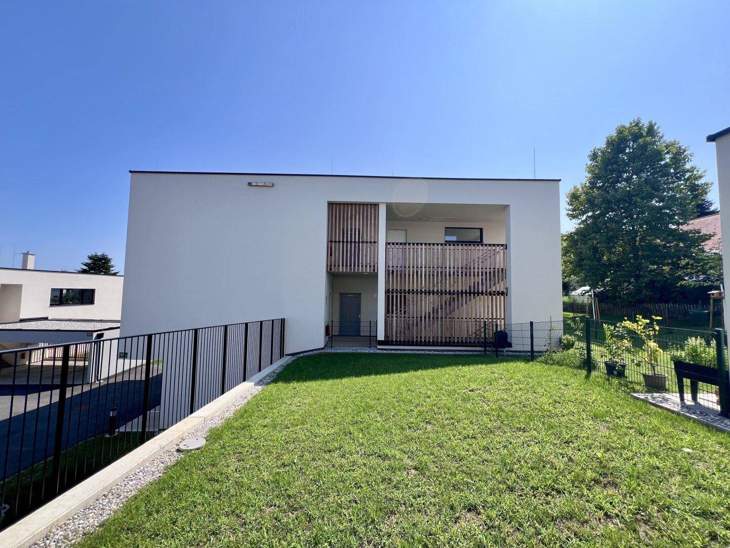 Rückseite eines modernen Gebäudes mit gepflegtem Rasen und Holzelementen an der Fassade.