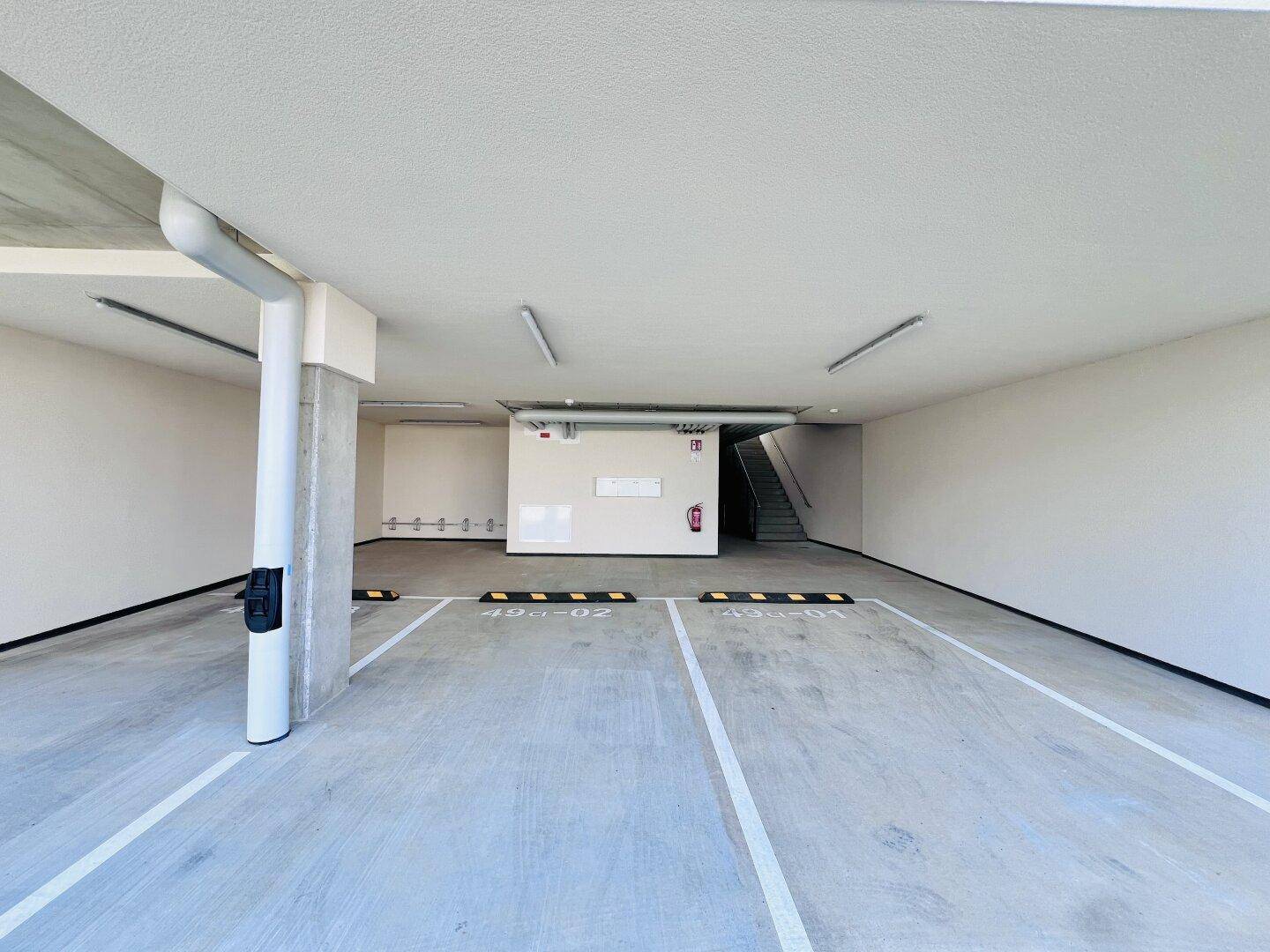 Geräumige Tiefgarage mit markierten Stellplätzen und Zugang zum Treppenhaus in einem Neubau.