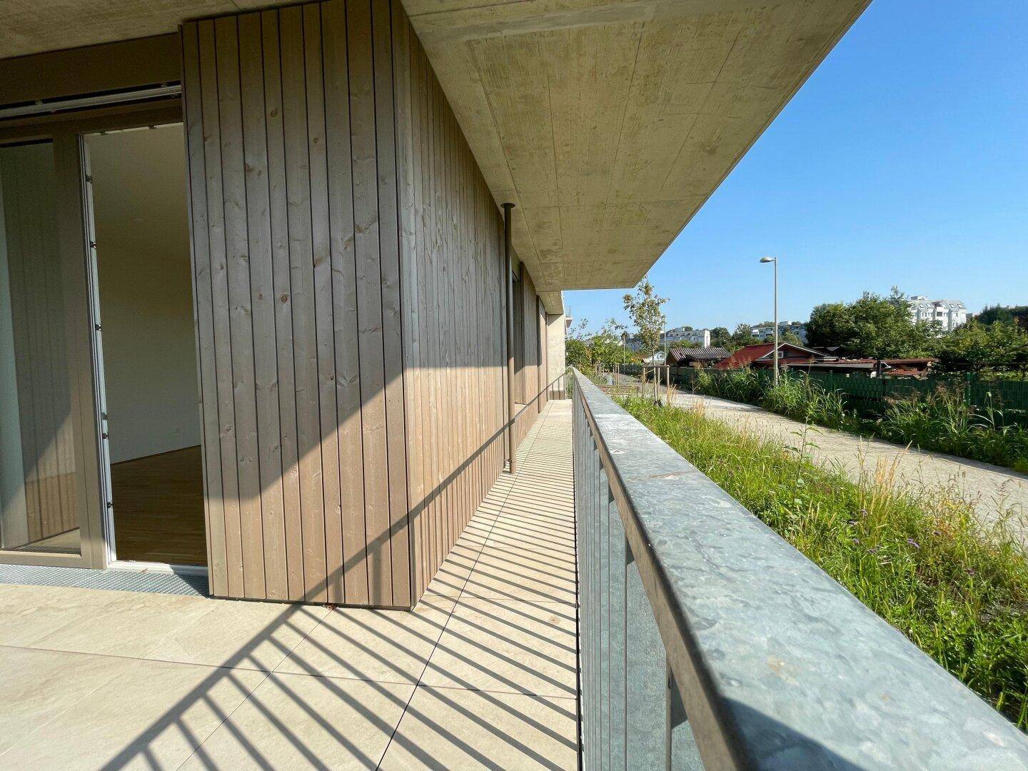 Langer Terrassenbereich mit Holzwänden und Zugang zu den Innenräumen, bei strahlendem Sonnenschein.