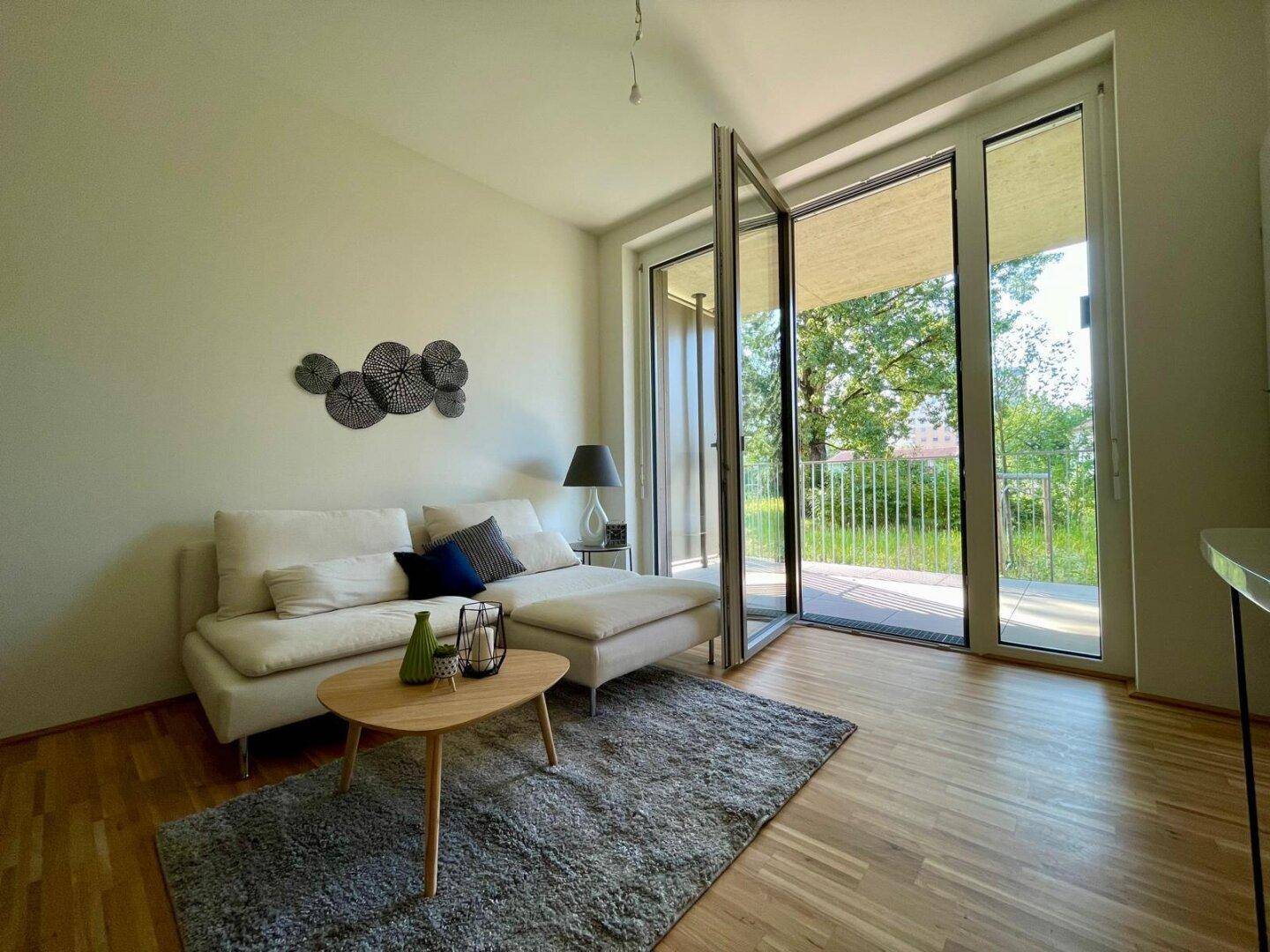 Gemütliches Wohnzimmer mit hellem Sofa, Holzboden und Zugang zu einem sonnigen Balkon.