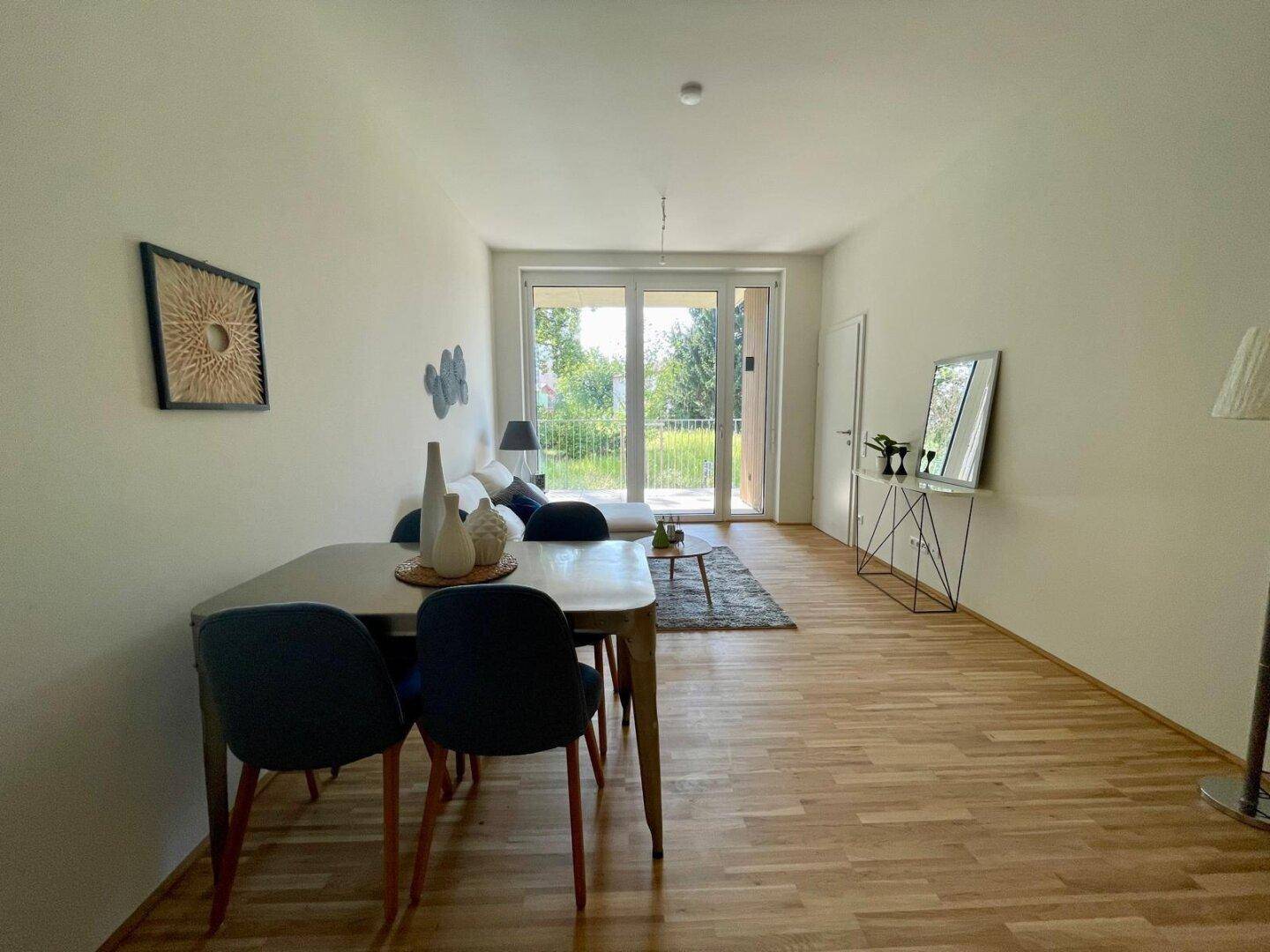 Offener Wohn-Essbereich mit Holzboden, Esstisch und gemütlicher Sitzecke mit Balkonzugang.
