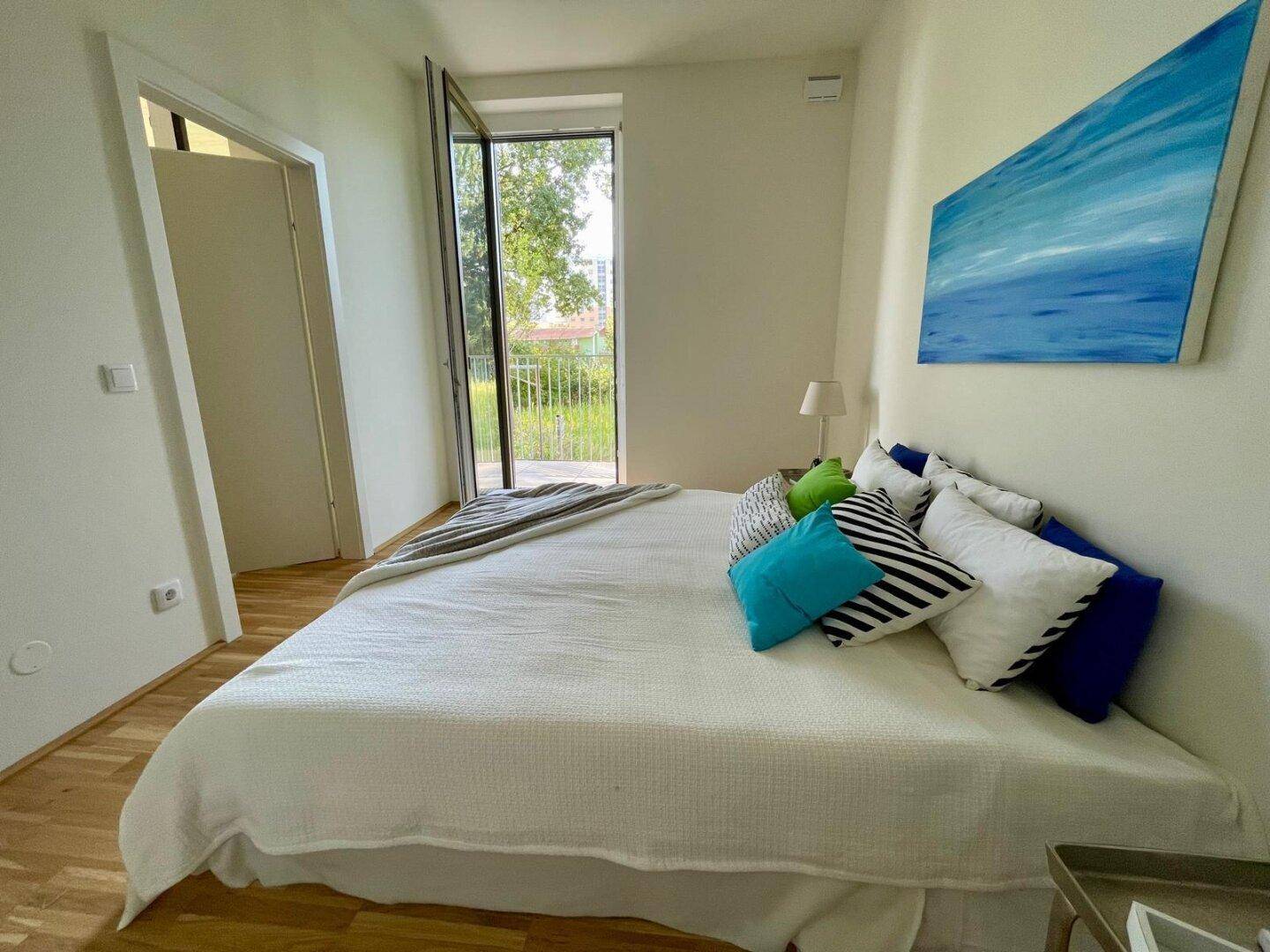 Helles Schlafzimmer mit Doppelbett, Holzboden und direktem Zugang zu einem Balkon.