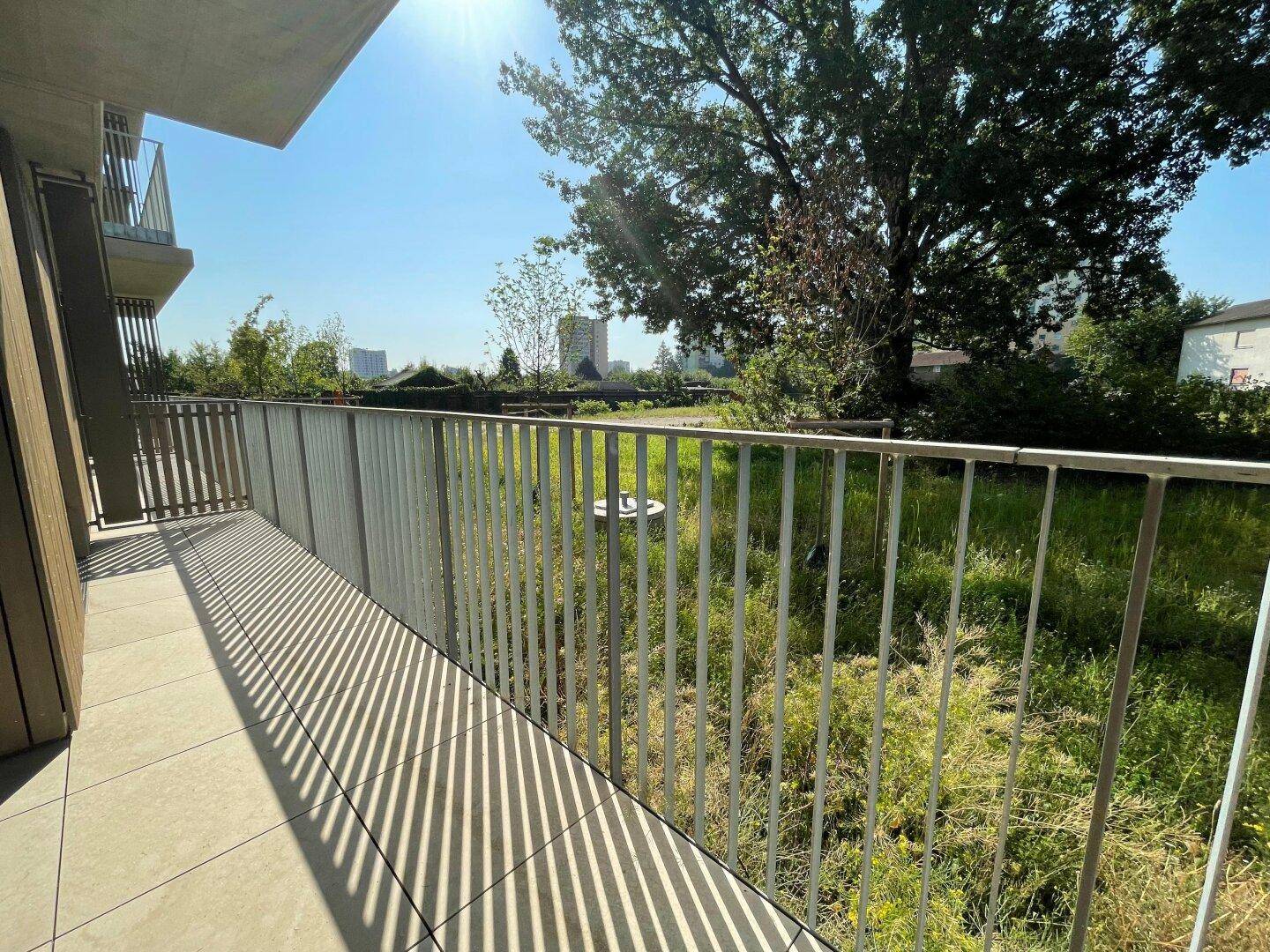 Sonniger Balkon mit Metallgeländer und weitem Blick über eine grüne Landschaft.