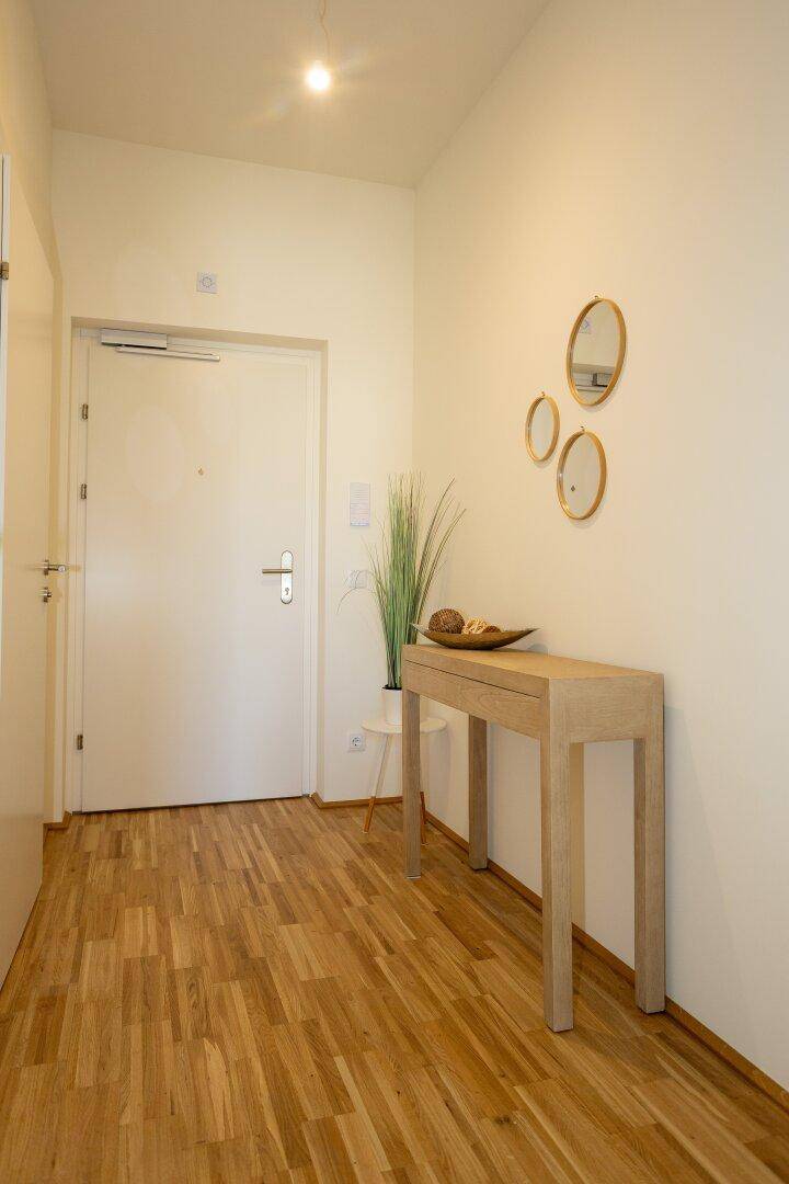Heller Eingangsbereich mit Holzparkettboden, einer schlichten Konsole und dekorativen Spiegeln.