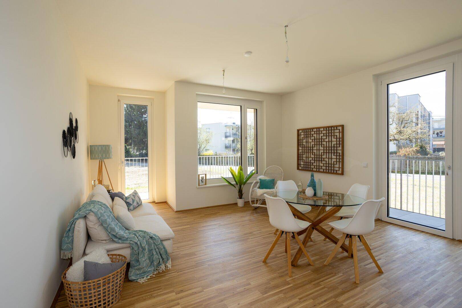 Geräumiger Wohn-Essbereich mit Holzparkett, großen Fenstern und Zugang zu einem Balkon.
