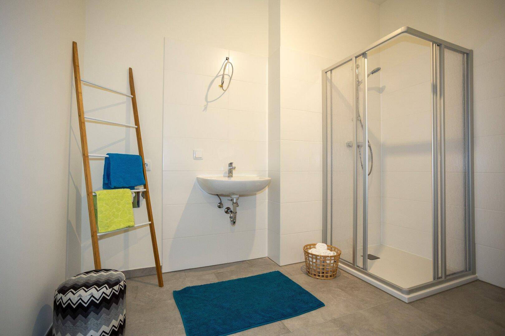 Modernes Badezimmer mit Duschkabine, Waschbecken und hellen Fliesen an den Wänden.