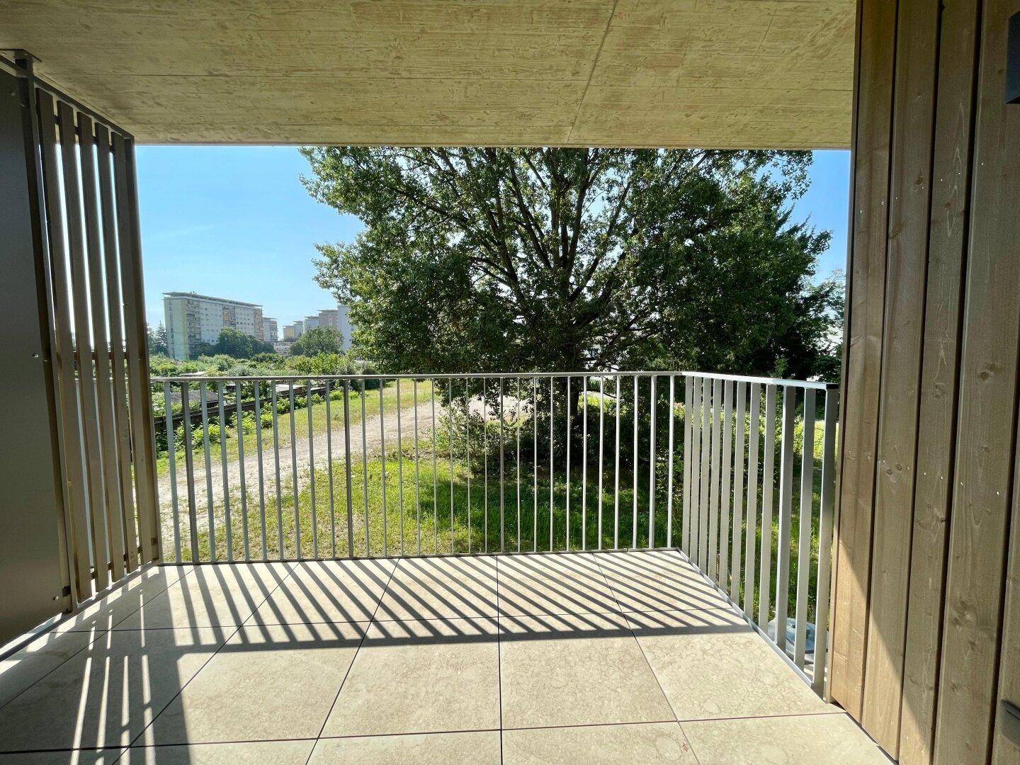 Balkon mit Fliesenboden und Blick auf die grüne Umgebung und weitere Gebäude.