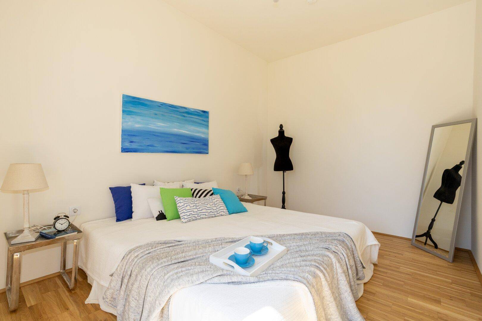 Schlafzimmer mit Holzboden, Doppelbett und farbigen Kissen, hell und freundlich.
