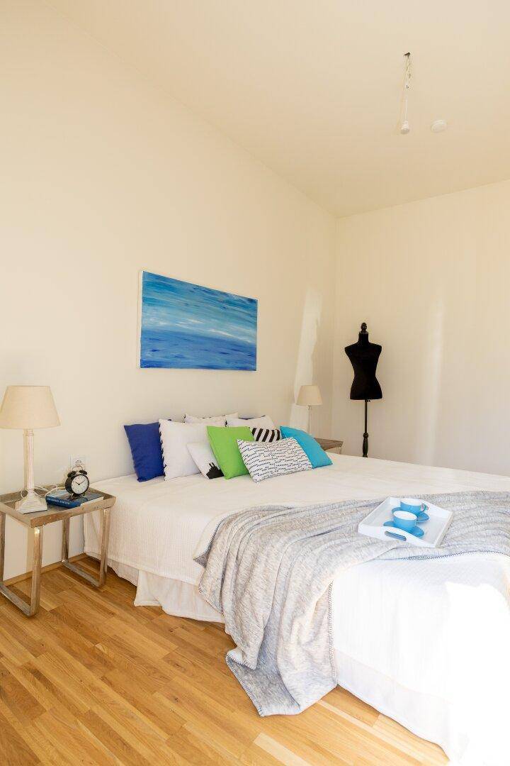 Helles Schlafzimmer mit Holzboden, großem Bett und farbigen Kissen.