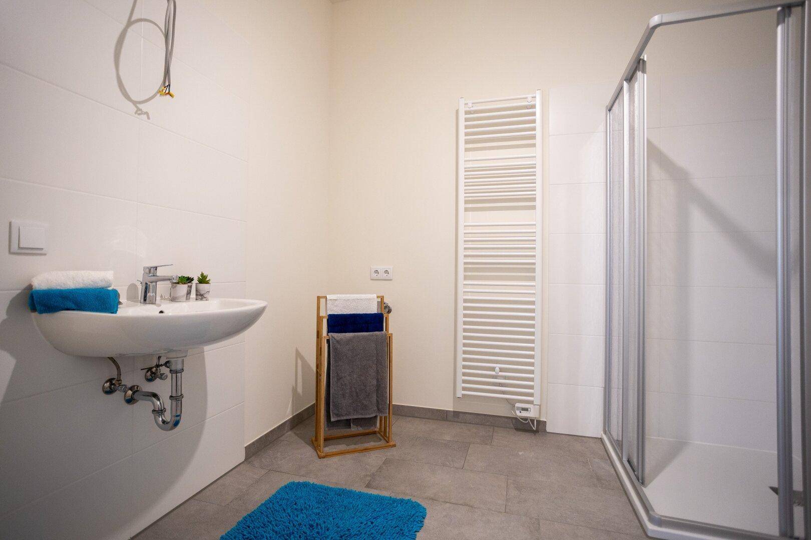 Modernes Badezimmer mit grauen Fliesen, Dusche, Einzelwaschbecken und Handtuchheizkörper.