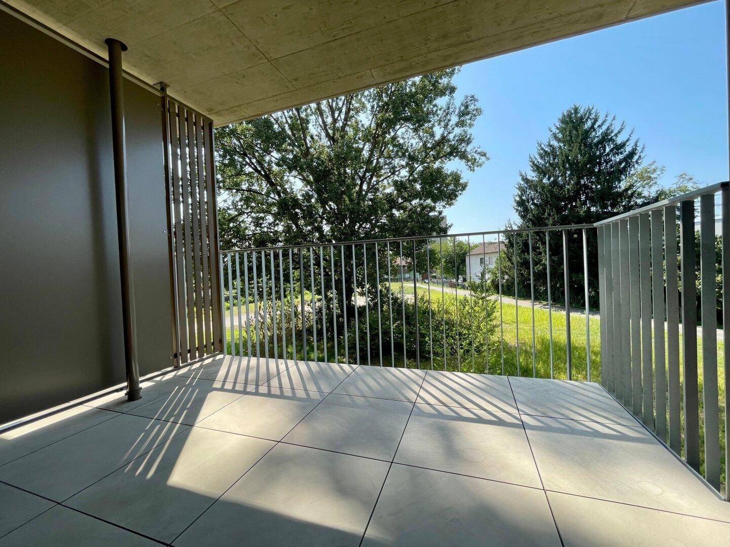 Geräumiger Balkon mit Fliesenboden und Blick auf grüne Bäume an einem sonnigen Tag.
