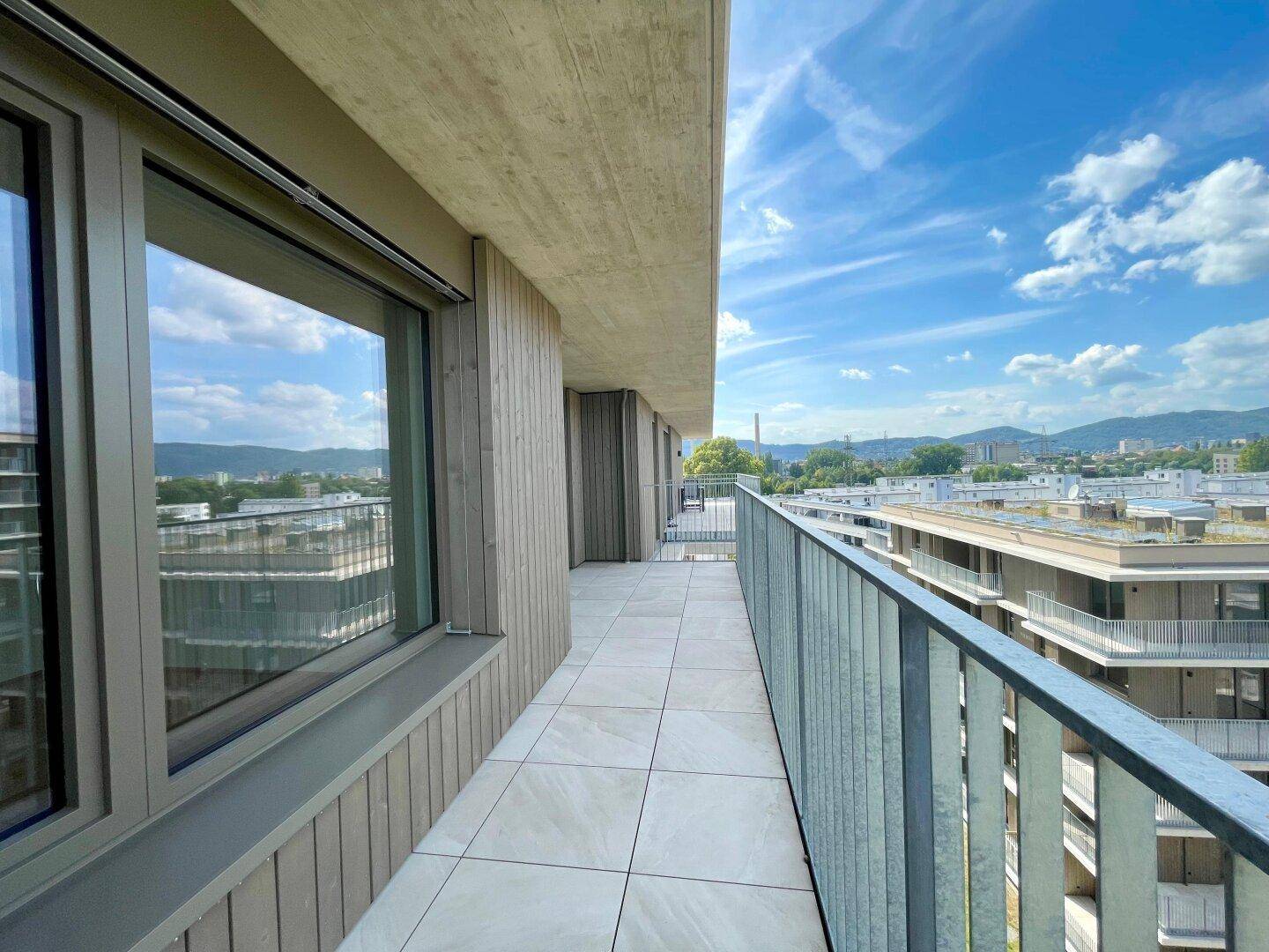 Heller Balkon mit moderner Holzfassade und Panoramablick auf die Umgebung und ferne Berge.