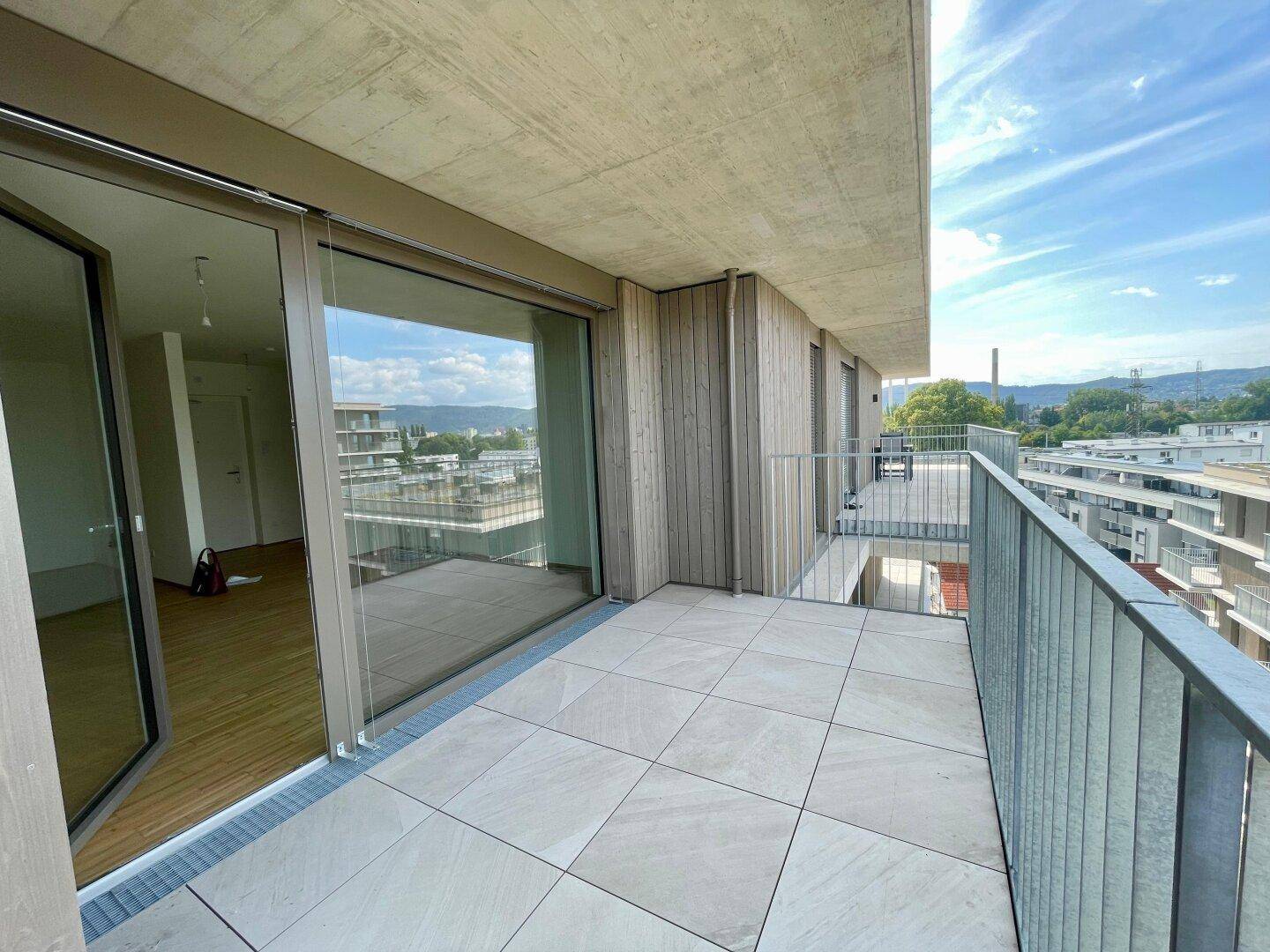 Geräumiger Balkon mit Fliesenboden und Blick auf die umliegenden Gebäude und die grüne Landschaft.
