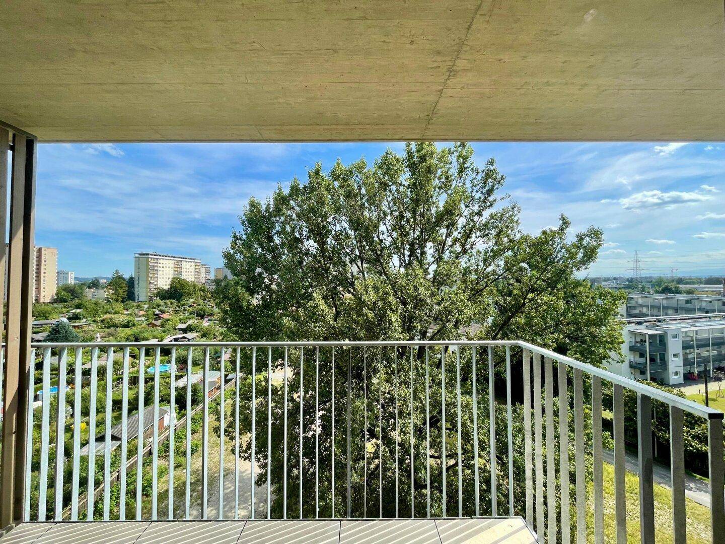 Heller Balkon mit Blick auf grüne Bäume und die umliegende Wohnbebauung.