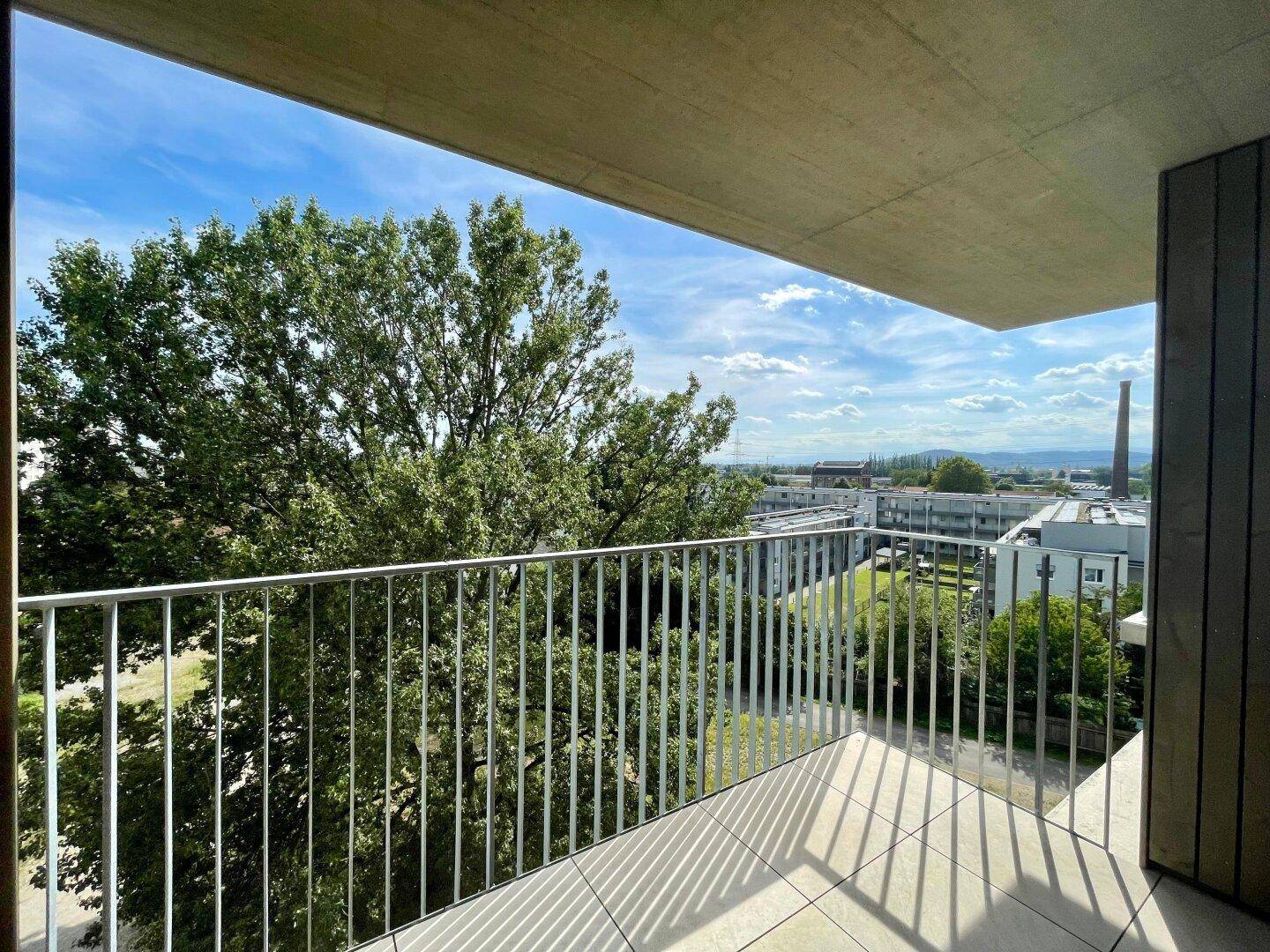Heller Balkon mit Blick auf grüne Bäume und die umliegende Wohnbebauung.