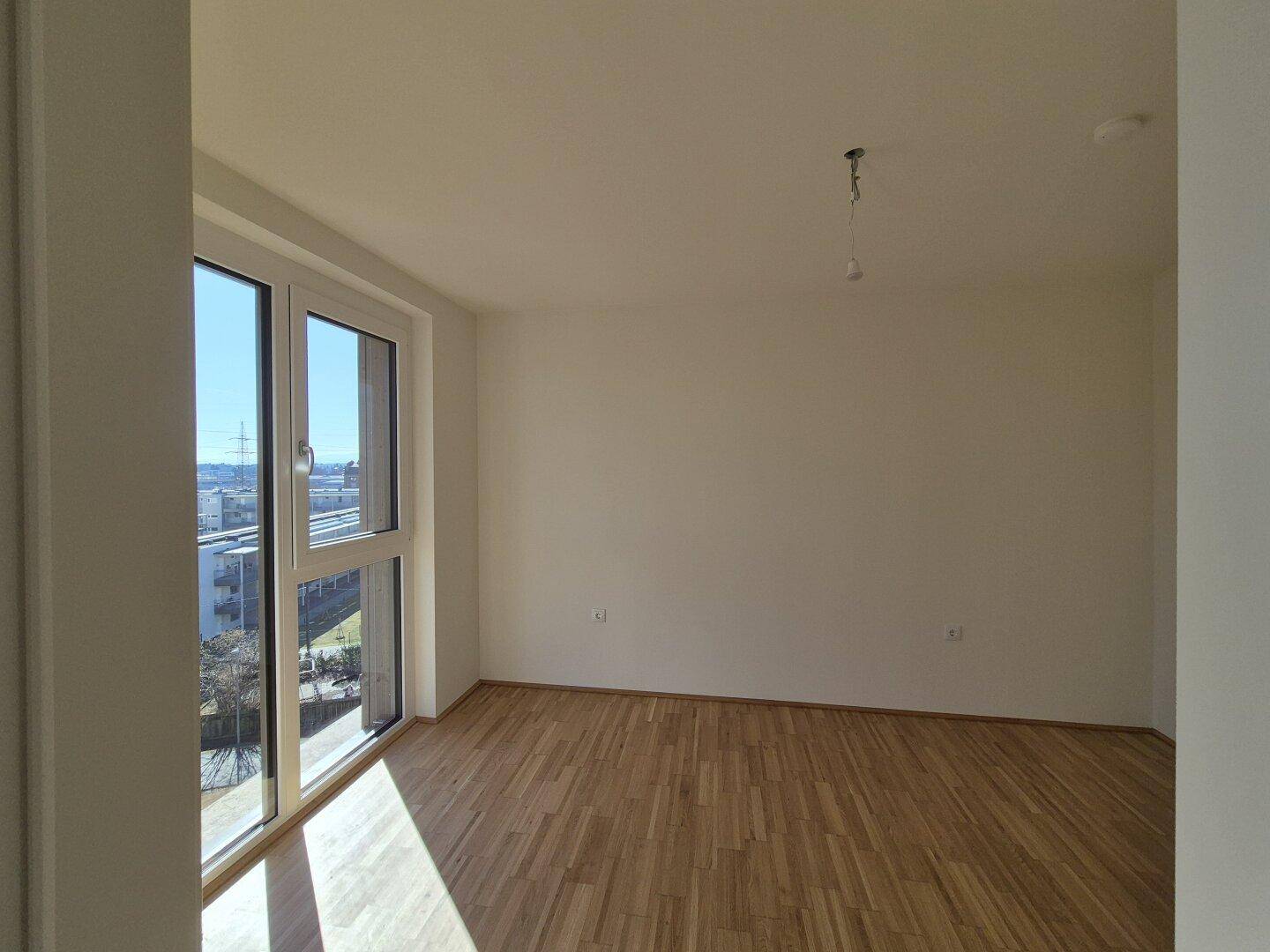 Heller Raum mit Holzboden und großen Fenstern, die viel Tageslicht hereinlassen.