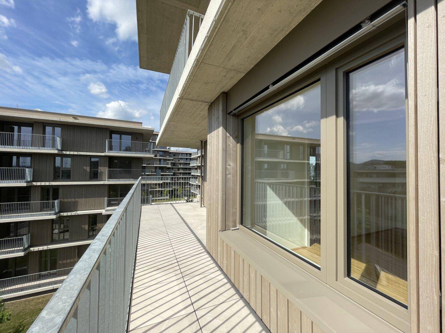 Geräumiger Balkon mit Fliesenboden und Blick auf die umliegenden Gebäude und den Himmel.