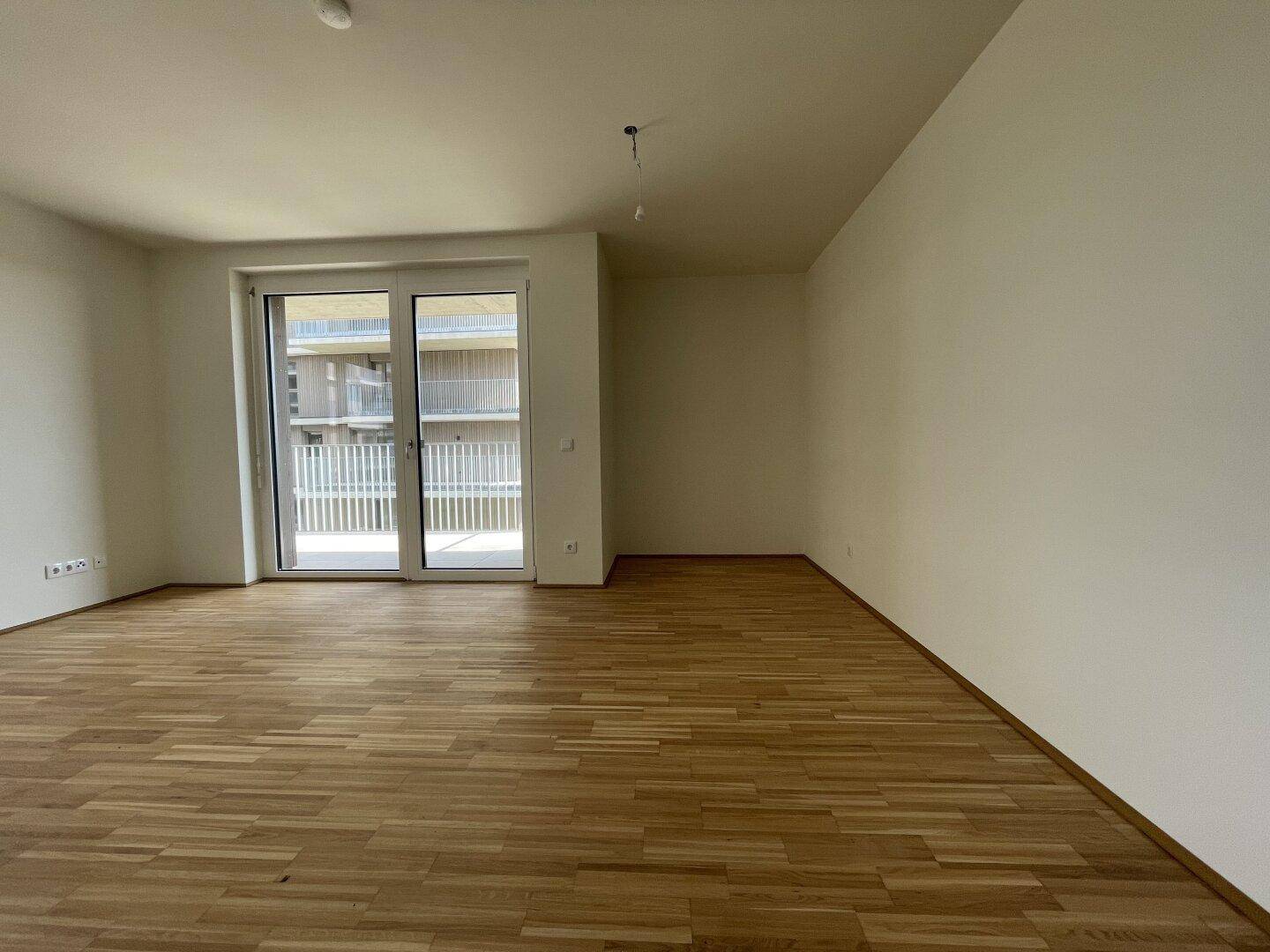 Geräumiges, leeres Zimmer mit Parkettboden und direktem Zugang zu einem Außenbereich.