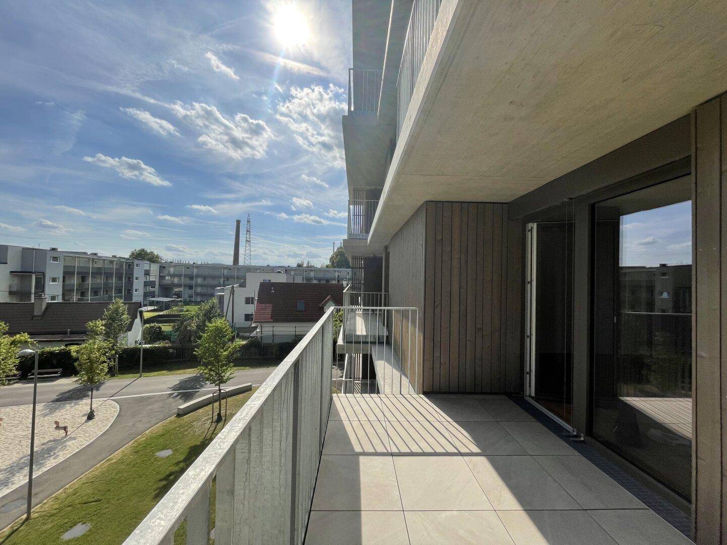 Sonniger Balkon mit Fliesenboden und Blick auf die Wohnanlage und einen Spielplatz.