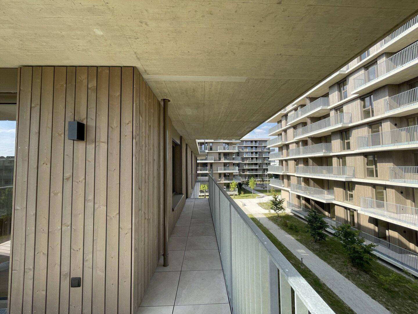 Langer Balkon mit Holzverkleidung und Fliesenboden, bietet einen Blick auf den Innenhof der Anlage.