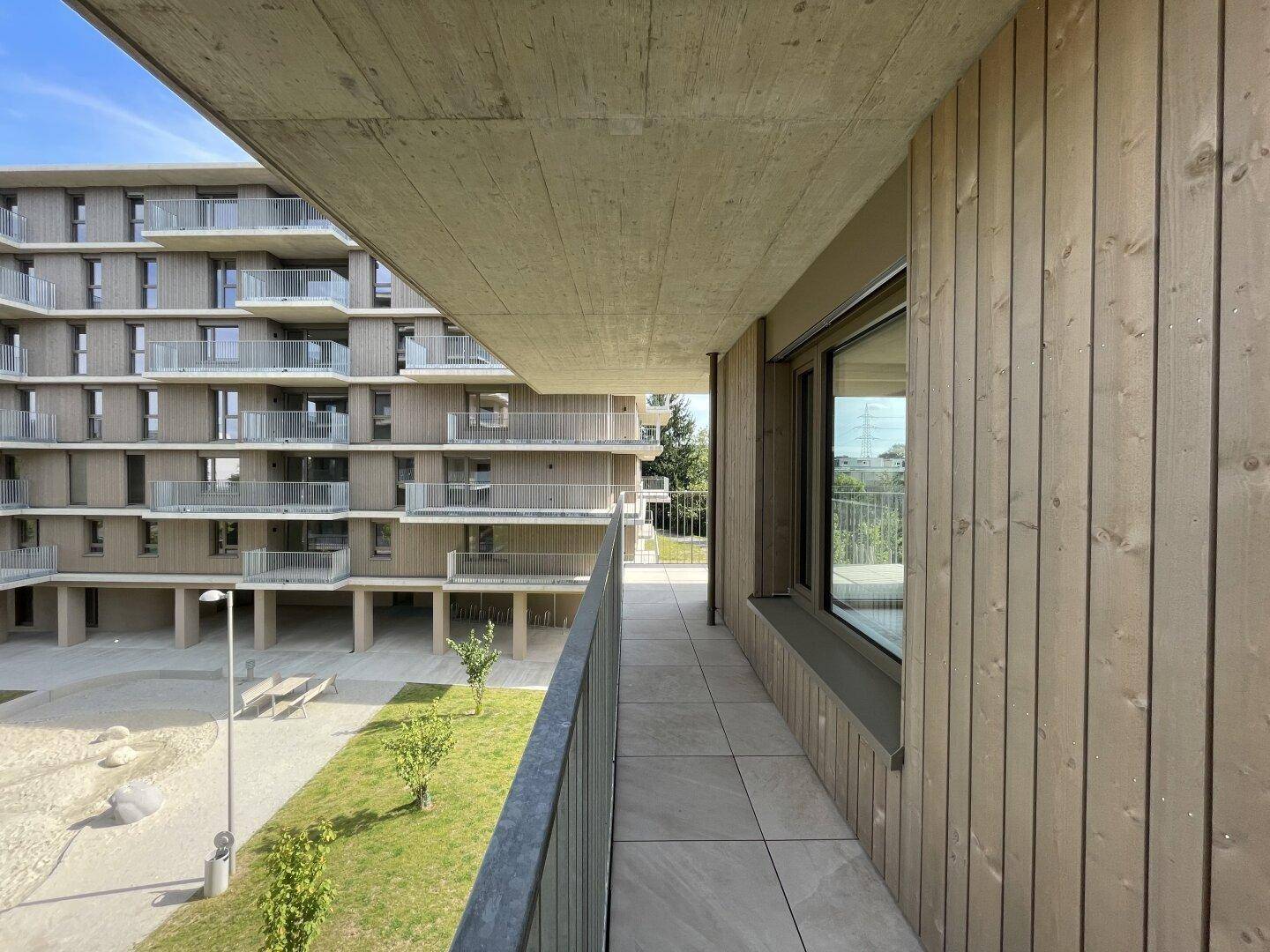 Balkon mit Fliesenboden und Holzverkleidung, mit Aussicht auf den begrünten Innenhof.