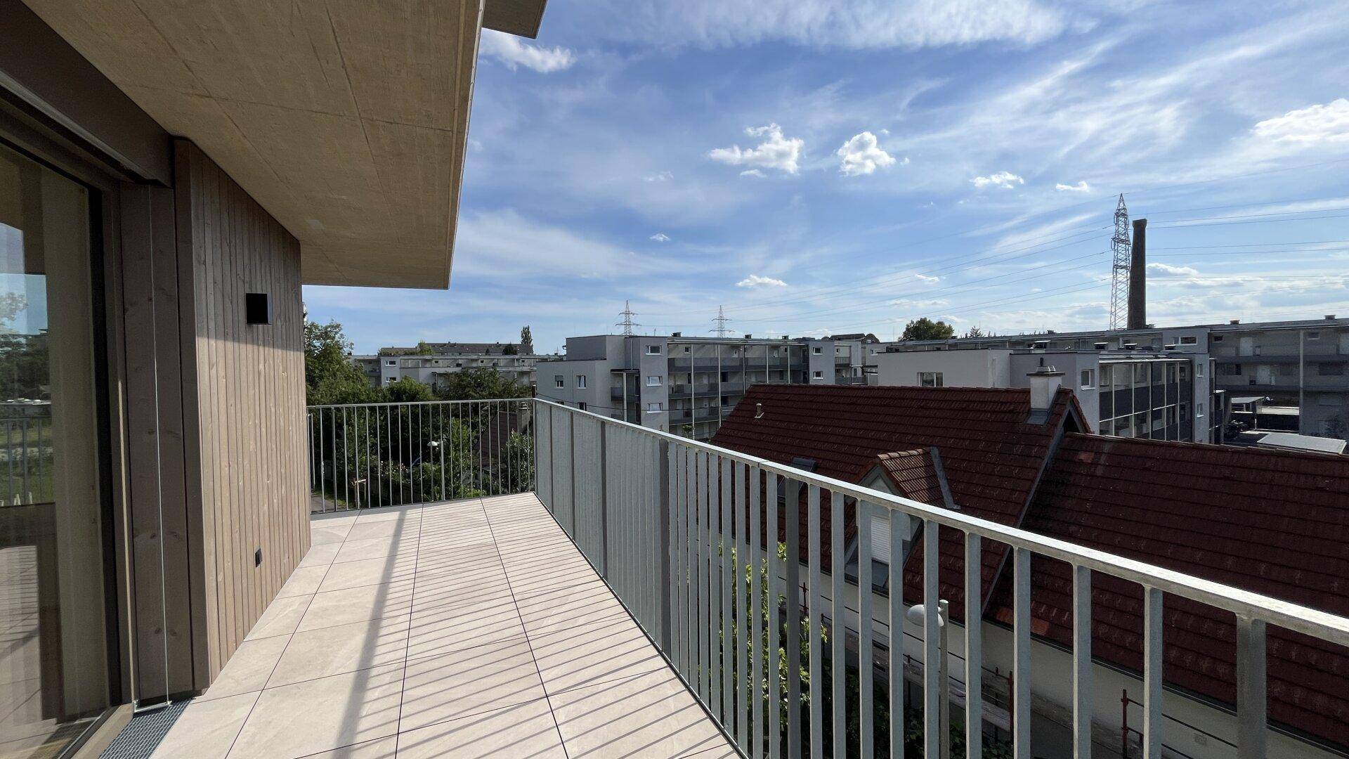 Geräumiger Balkon mit Fliesenboden und Blick auf die umliegende Bebauung und den Himmel.