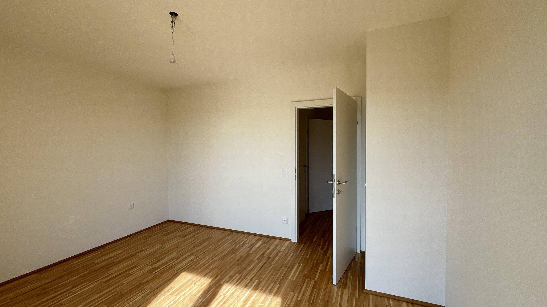 Sonniges Zimmer mit Parkettboden und weiß gestrichenen Wänden, ideal als Schlaf- oder Arbeitszimmer.